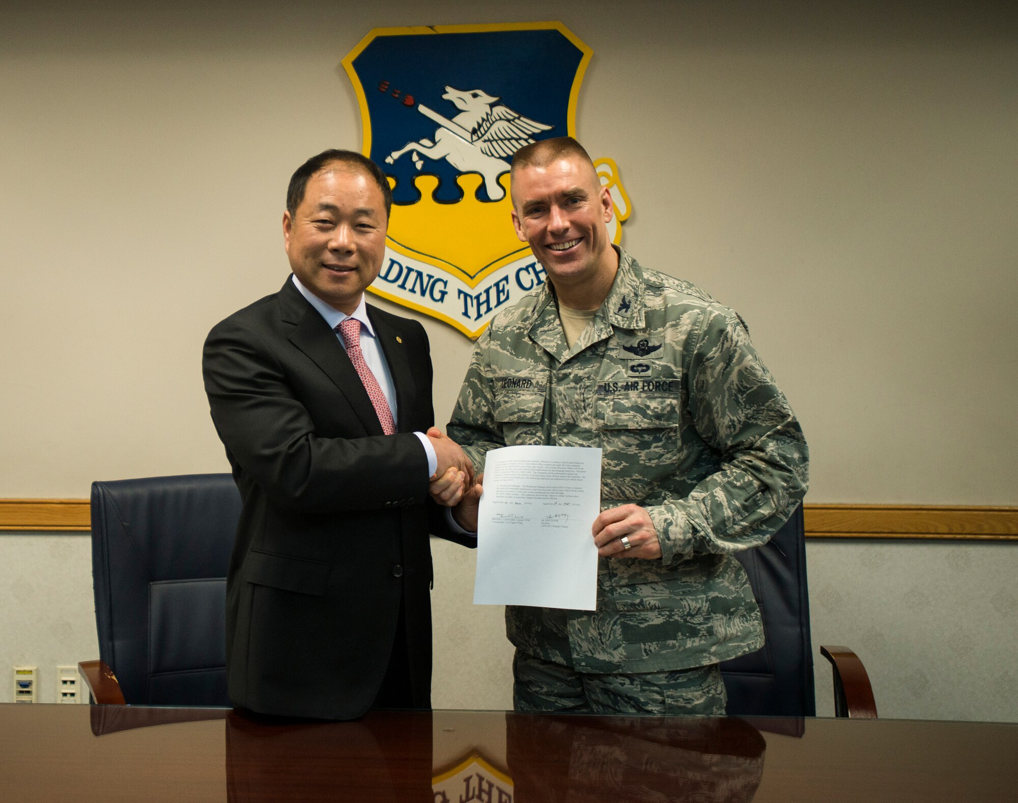 Kim In Sok, KEU president, and Col. Brook Leonard, 51st Fighter Wing commander, shake hands after signing an agreement to increase the number of vehicle authorizations for Korean National employees March 18, 2014, at Osan Air Base, Republic of Korea. The agreement will increase the number of vehicle authorization from 300 to 350 and also standardizes base access hours for Korean National employees from the hours of 5 a.m - 8 p.m. (U.S. Air Force photo by Staff Sgt. Jake Barreiro)