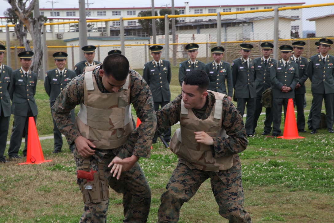 U.S. Marines Cpl. Ivan Luna, left, and Lance Cpl. Luis R. Riveramendez demonstrate a Marine Corps Martial Arts Program defensive technique to officer candidates of the Japan Ground Self-Defense Force at Camp Schwab Feb. 27 during a tour of 4th Marine Regiment as part of the Japan Observer Exchange Program. The Marines demonstrated several techniques from each belt level of MCMAP to help explain the hand-to-hand combat skills used by Marines. Luna is a field wireman with 3rd Battalion, 3rd Marine Regiment, 3rd Marine Division, III Marine Expeditionary Force. Riveramendez is an intelligence specialist with 4th Marines, 3rd Marine Division, III MEF.