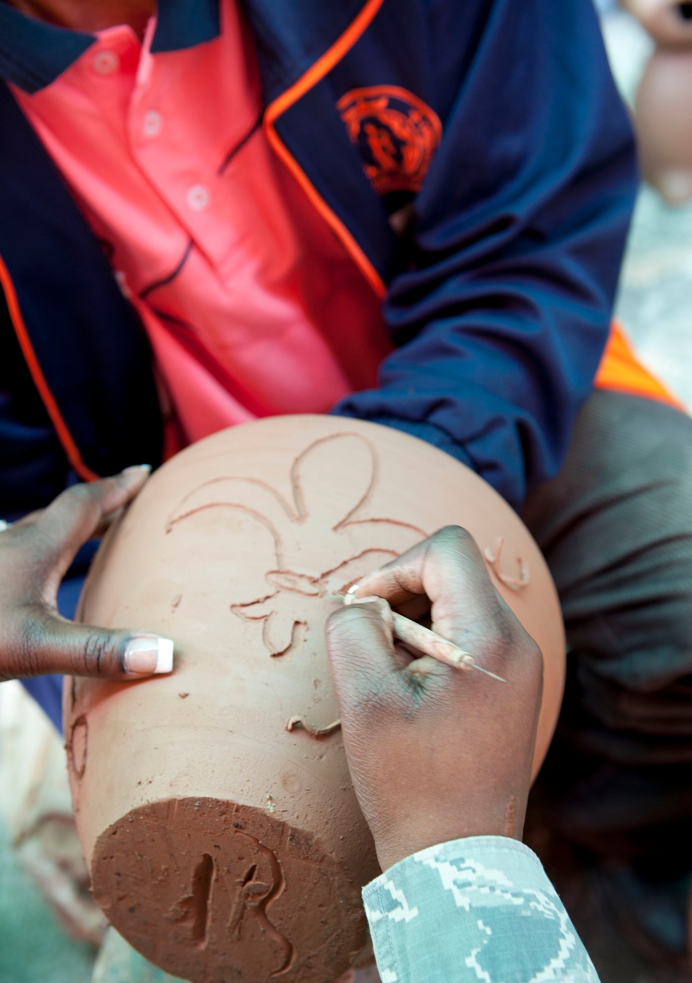 Tech. Sgt. Kelly Hughes with the Louisiana Air National Guard etches the New Orleans fleur-de-lis into a clay pot in a ceramics demonstration at Dan Kwian Witthaya School in Korat, Thailand. U.S., Thai and Singapore Air Force members were at the school for a day of community service during exercise Cope Tiger 2014, offering medical services and exchanging culture with the students and locals from the Dan Kwian village area. The village is famous in the region and internationally for the unique and beautiful pottery it crafts from the black, bronzed clay of the Moun River. (U.S. Air Force photo by 2Lt. Michael Harrington/Released)