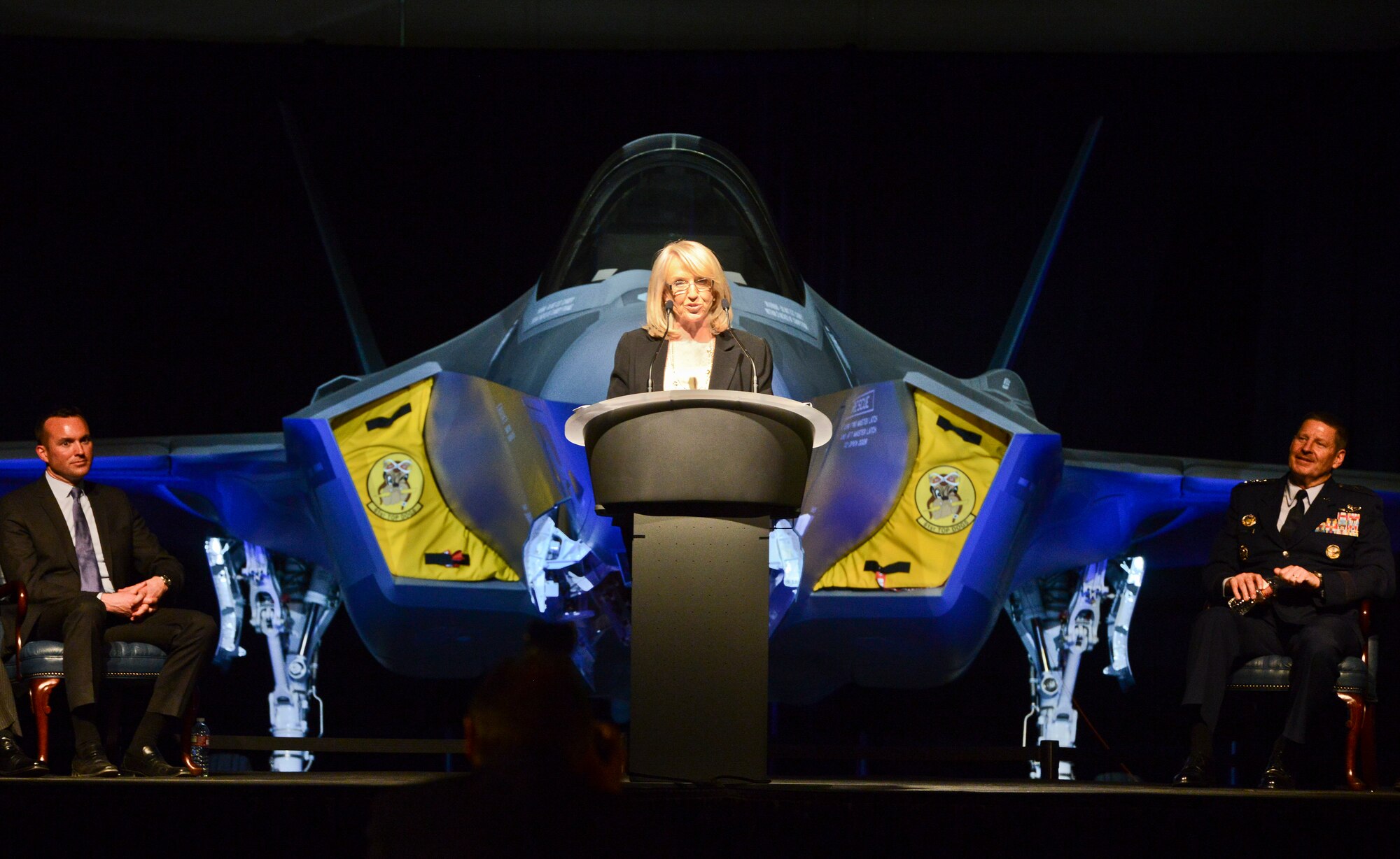 Arizona Governor Jan Brewer addresses an audience of approximately 500 community leaders, elected officials, representatives from partner nation air forces and Luke Airmen during an unveiling ceremony on March 14 at Luke Air Force Base for the 56th Fighter Wing’s first F-35 Lightning II fighter jet. Brewer was joined on stage by Undersecretary of the Air Force Eric Fanning (left) and Gen. Robin Rand, commander of Air Education and Training Command (right). “I am thrilled for all the military, for the residents of the West Valley and for our state,” the governor said. “I’m immensely proud to stand with you to welcome this incredible aircraft to the Valley of the Sun.” (U.S. Air Force photo by Senior Airman Devante Williams)