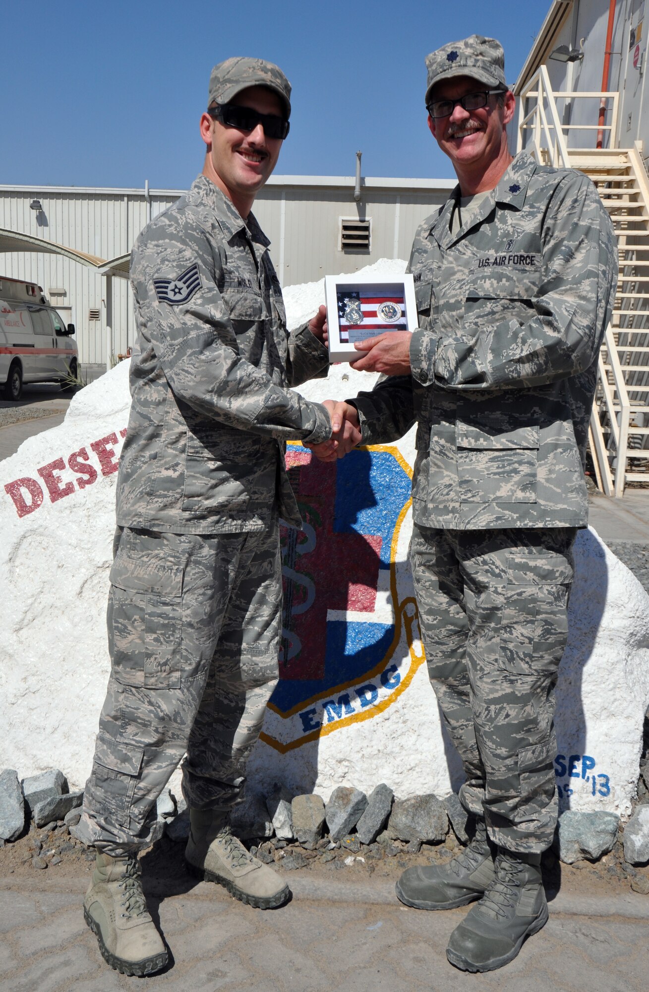 Air Force Staff Sgt. James Worley, 380th Expeditionary Security Forces Squadron kennel master, presents a plaque to Air Force Lt. Col. Mark Lehman, 380th Expeditionary Medical Group Preventive Health flight commander, as a token of gratitude for his assistance in care with the military working dogs deployed to the 380 ESFS March 17, 2014. (U.S. Air Force photo by Master Sgt. April Lapetoda/Released)