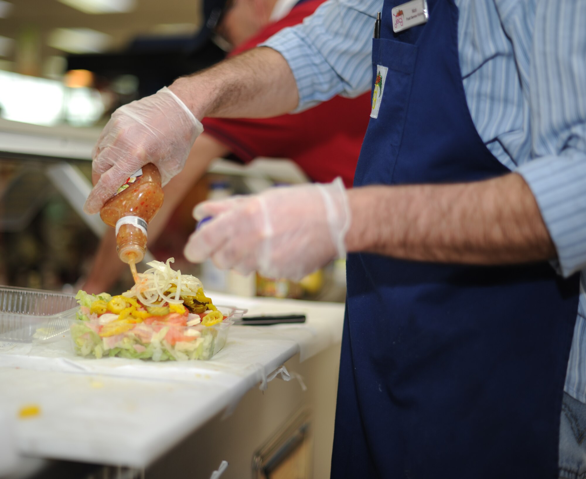 Nick Constance, a food service worker, pours dressing on a salad at the commissary deli at Spangdahlem Air Base, Germany, March 18, 2014. The commissary offers the deli service to all Department of Defense ID cardholders and their dependents. (U.S. Air Force photo by Airman 1st Class Dylan Nuckolls / Released) 