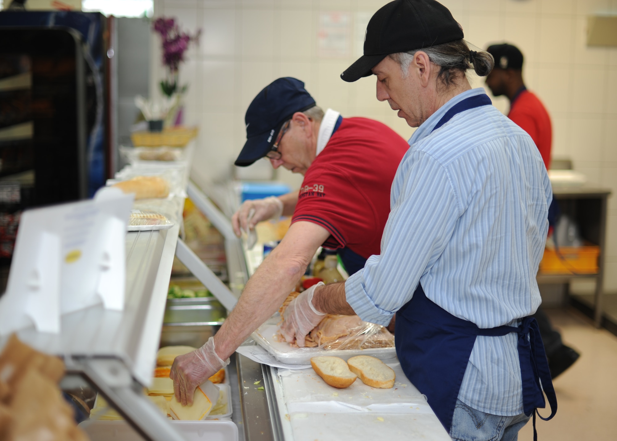Food service workers select ingredients for customer-ordered sandwiches at the commissary deli at Spangdahlem Air Base, Germany, March 18, 2014. Food service workers process hundreds of sandwich orders each day, particularly during the lunch rush. (U.S. Air Force photo by Airman 1st Class Dylan Nuckolls / Released) 