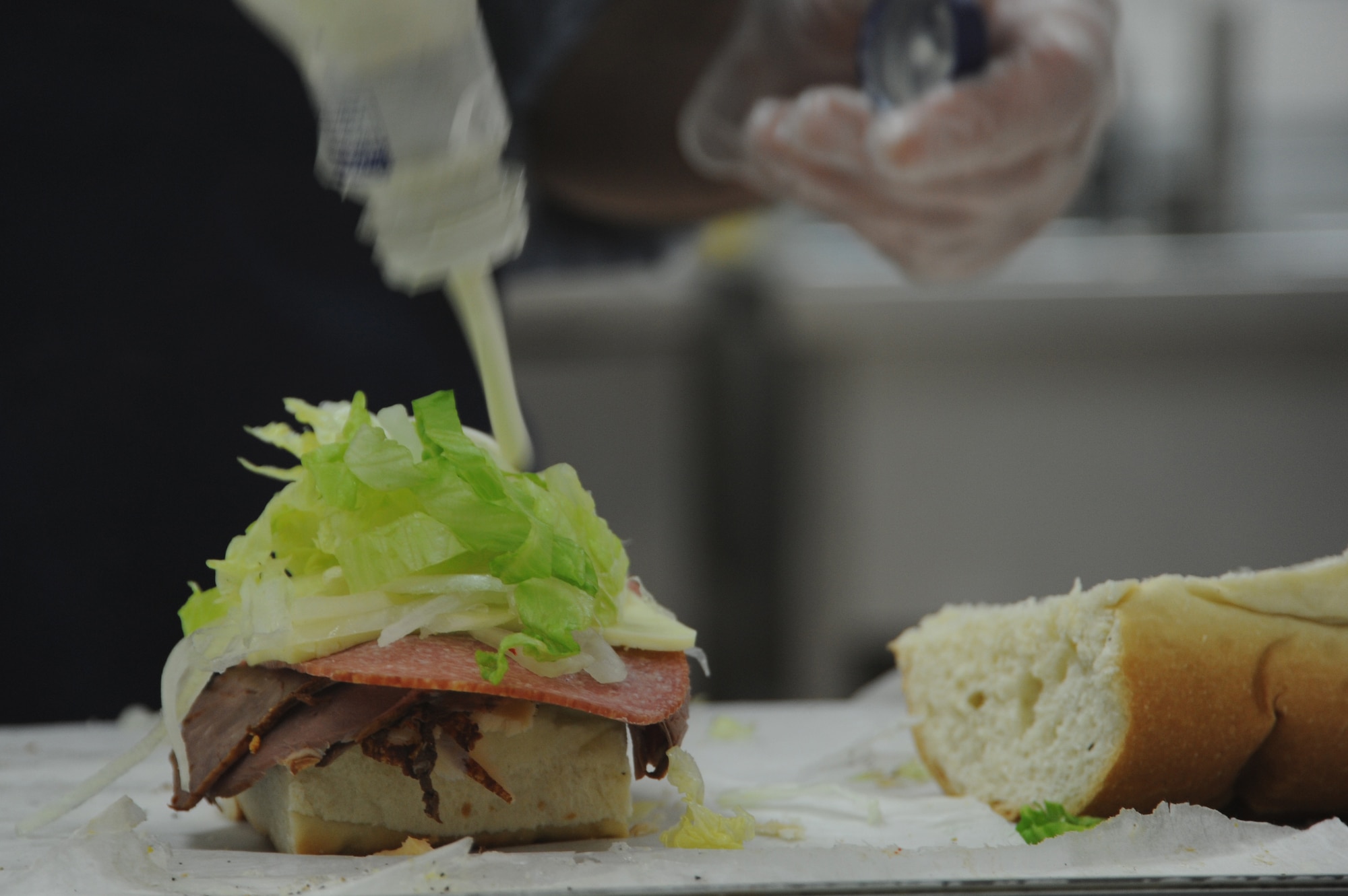 Nick Constance, a food service worker, pours mayonnaise on a sandwich at the commissary deli at Spangdahlem Air Base, Germany, March 18, 2014. Customers can select a variety of meats, cheeses, breads and condiments to personalize for their sandwiches. (U.S. Air Force photo by Airman 1st Class Dylan Nuckolls/Released) 