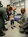 Capt. Jenny Miller, 535th Airlift Squadron C-17 pilot, (left) assists Master Sgt. Galen Ho, 154th Operations Support Squadron Aircrew Flight Equipment NCO in charge, (right) with putting a hanging harness on Kaitlin Blackmon as part of a Girl Scout tour on Joint Base Pearl Harbor-Hickam, Hawaii, March 17, 2014. Kaitlin joined 26 fellow Brownie Girl Scouts for a “pilot for-a-day” style career day hosted by the 15th Operations Group, in order to earn the Air Force Pride Badge. (U.S. Air Force photo/Tech. Sgt. Terri Paden)