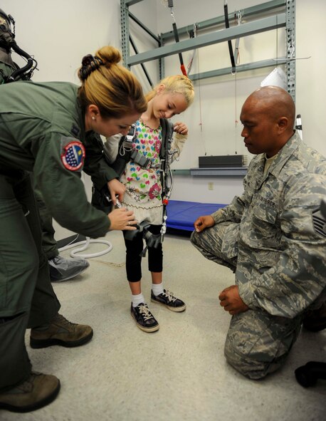 Capt. Jenny Miller, 535th Airlift Squadron C-17 pilot, (left) assists Master Sgt. Galen Ho, 154th Operations Support Squadron Aircrew Flight Equipment NCO in charge, (right) with putting a hanging harness on Kaitlin Blackmon as part of a Girl Scout tour on Joint Base Pearl Harbor-Hickam, Hawaii, March 17, 2014. Kaitlin joined 26 fellow Brownie Girl Scouts for a “pilot for-a-day” style career day hosted by the 15th Operations Group, in order to earn the Air Force Pride Badge. (U.S. Air Force photo/Tech. Sgt. Terri Paden)