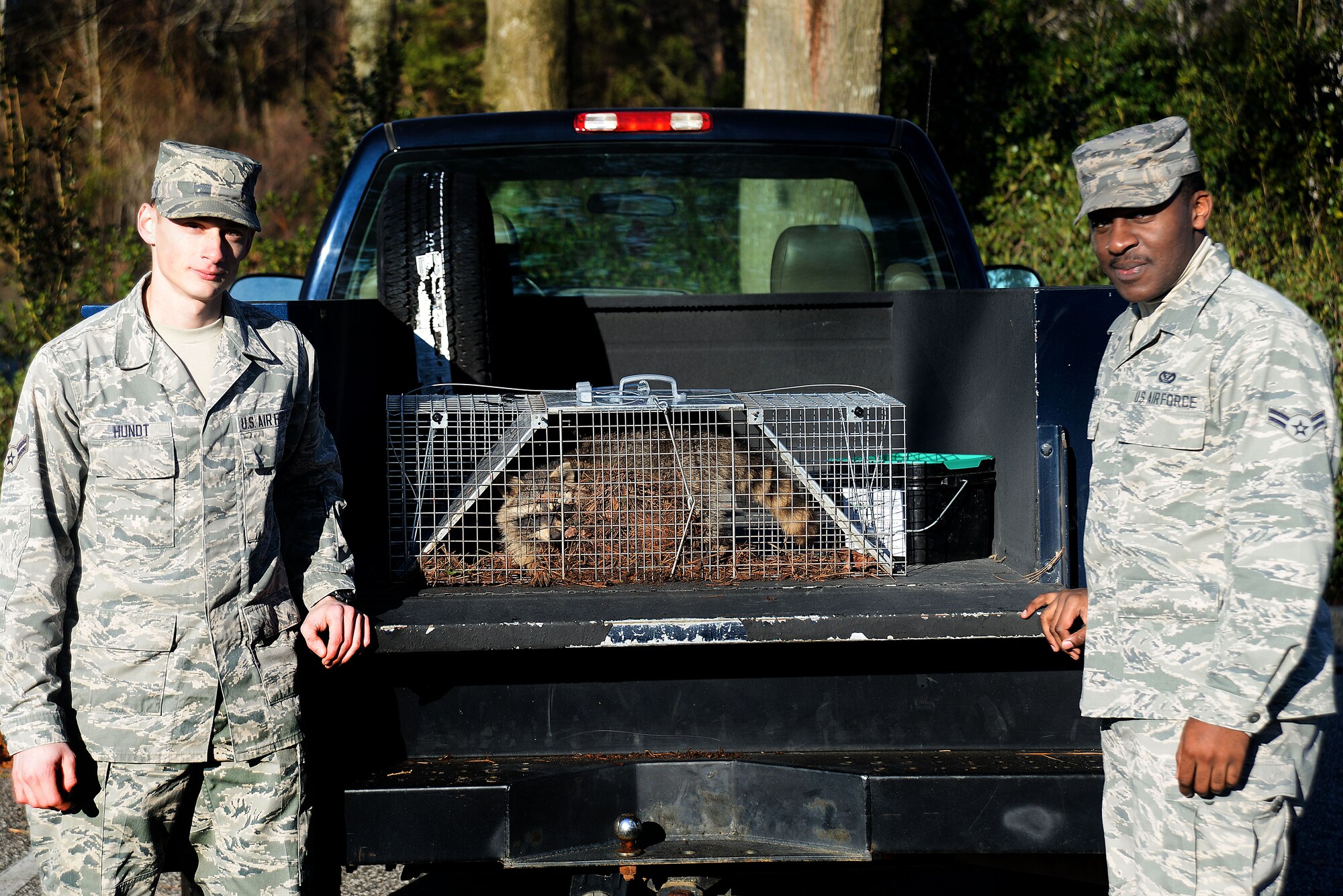 [Left to right] U.S. Air Force Airmen 1st Class Colin Hundt and Valerie Shinwen, 20th Civil Engineer Squadron pest management specialists, pose with a captured raccoon, Shaw Air Force Base, S.C., Feb. 27, 2014. The trap was set two days prior to the capture of the raccoon. (U.S. Air Force photo by Airman 1st Class Michael A. Cossaboom/Released)