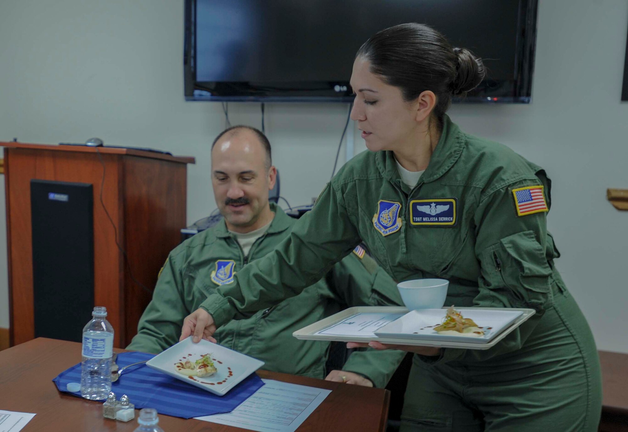 Tech. Sgt. Melissa Derrick, 65th Airlift Squadron flight attendant, serves Col. Michael Merritt, 15th Operations Group commander, a plate of sea bass in the 65 AS conference room on Joint Base Pearl Harbor-Hickam, Hawaii, March 19, 2014. The dish was served as part of a seven-course Joint Service Flight Culinary Training Meal. The flight culinary training meals are part of an ongoing effort between the two services to maximize on-the-job training opportunities and increase camaraderie and cross-flow of communication between the units. (U.S. Air Force photo/Tech. Sgt. Terri Paden)