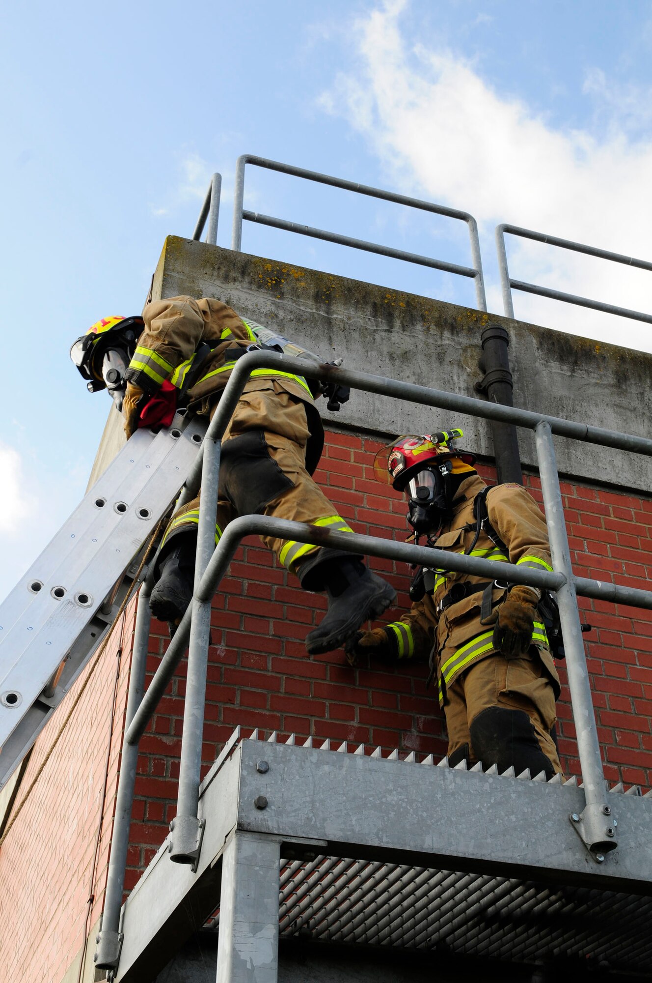 Defence Fire Service Firefighter Paul Cusden, left, from Ramsgate, Kent, and DFS Crew Manager Chris Gould, from Acle, Norfolk, both 100th Civil Engineer Squadron Fire Department firefighters, make their way to the top of the fire training house March 18, 2014, during live-fire training on RAF Mildenhall, England. The simulated house provides a variety of fire hazards, enabling the firefighters to practice and hone their live-saving skills for different situations. The difference between the upstairs and downstairs training is the way the firefighters make entry. The technique to fight the fire is the same, but they use a ladder to gain access to the upper level. While one crew attacks the fire downstairs, another crew ladders the facility, locates the fire and attacks it on the second level. Everything on scene is relayed to the incident commander, and the incident safety officer continuously observes the scene and firefighter actions, ensuring overall safety on scene. (U.S. Air Force photo by Karen Abeyasekere/Released)
