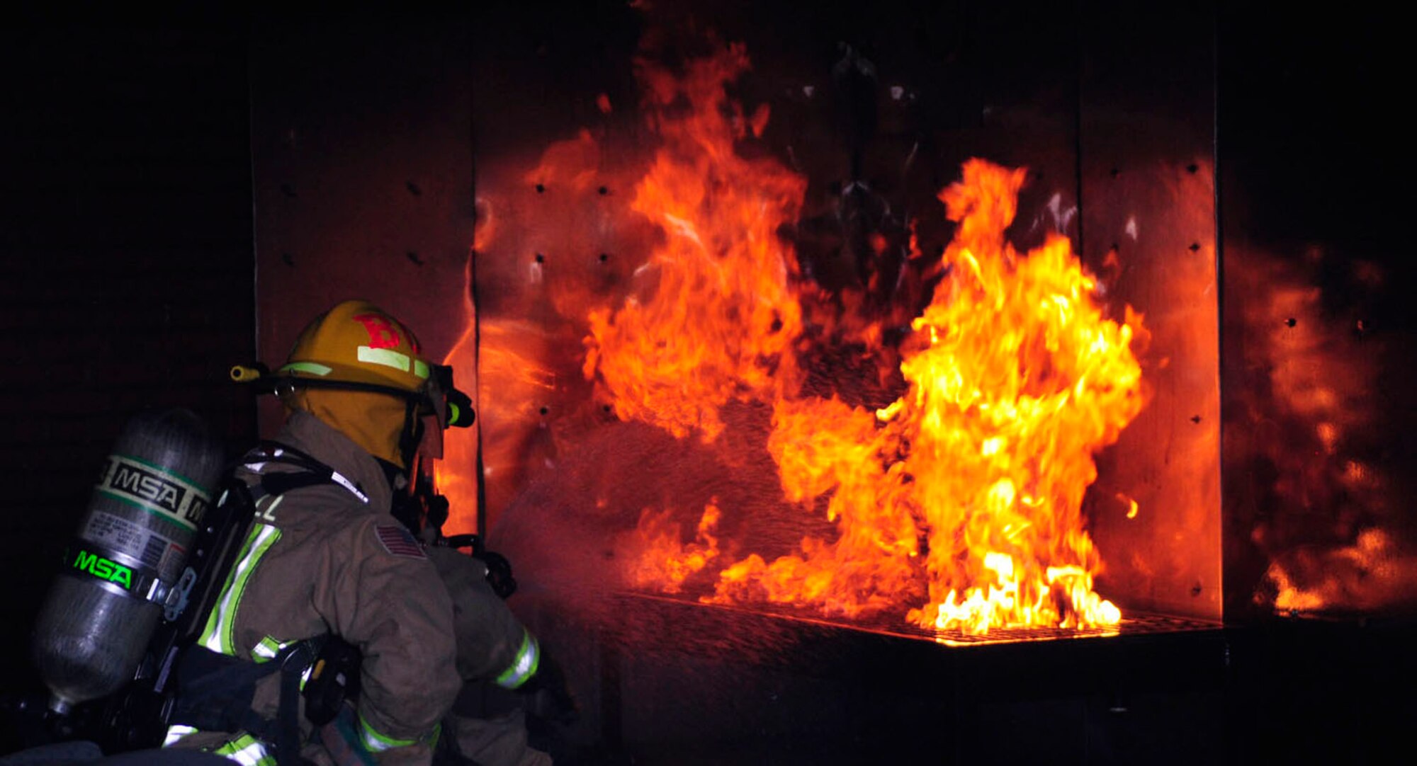 U.S. Air Force Airman William Burden, from Scott Depot, W. Va., and Defence Fire Service Firefighter Paul Cusden, from Ramsgate, Kent, both 100th Civil Engineer Squadron Fire Department firefighters, attack a simulated furniture fire using proper extinguishing techniques to prevent flashovers March 18, 2014, at the fire training area on RAF Mildenhall, England. The fire department's live-fire training requirement involves performing two structural and two aircraft live-fire burns per year. The training is vital in ensuring firefighters learn and practice proper firefighting techniques. It also teaches them to recognize firsthand the importance of personal protective equipment within a live-fire environment, as well as requirements to keep them as safe as possible while on the scene. (U.S. Air Force photo by Karen Abeyasekere/Released)