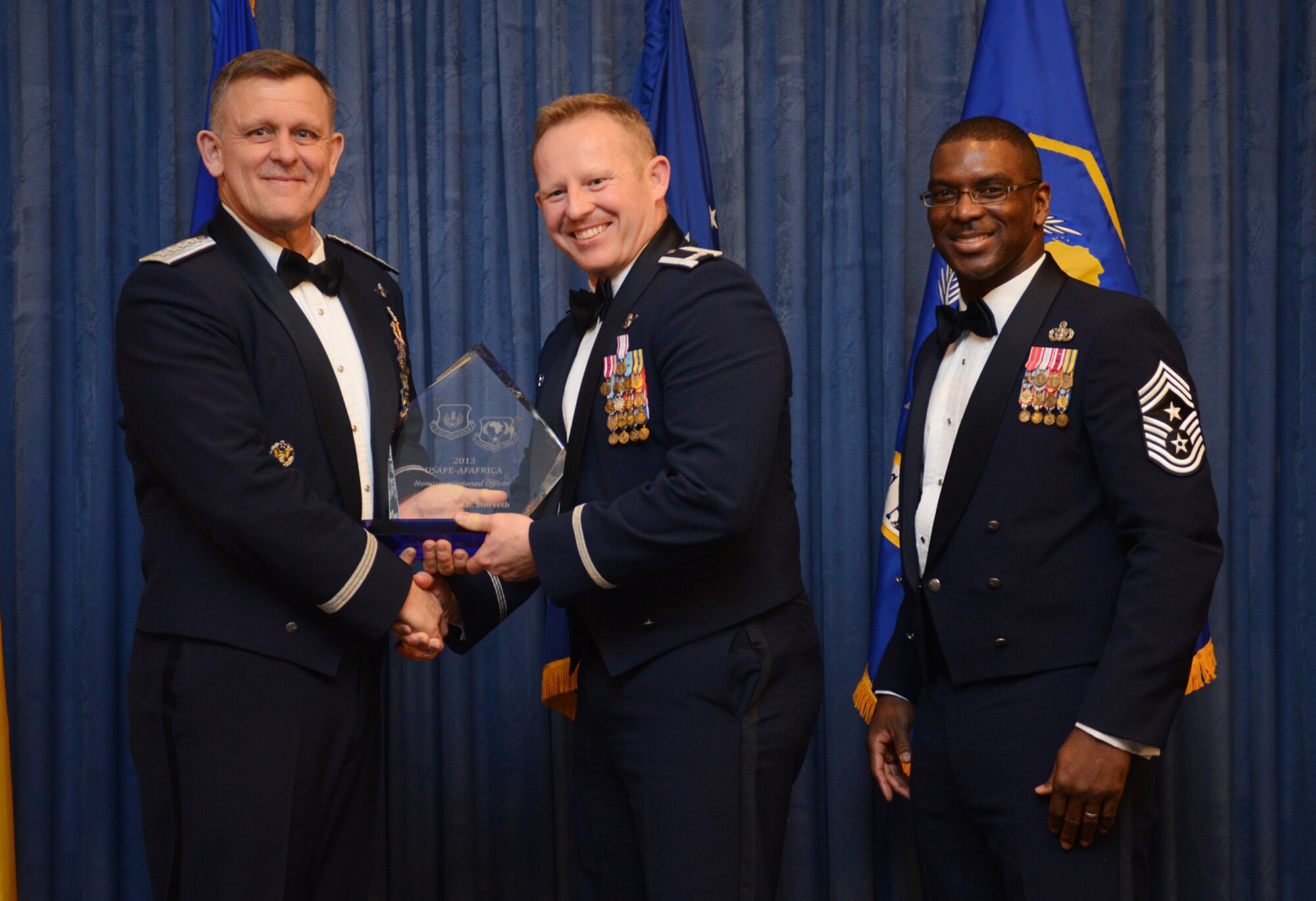 Col. Joseph McFall, 435th Air Ground Operations Wing commander, accepts the U.S. Air Forces in Europe and Air Forces Africa NCO of the Year award on behalf of Tech. Sgt. Douglas Storseth, 1st Combat Communications Squadron NCO in charge of plans, who is currently deployed to Africa, from Gen. Frank Gorenc, USAFE-AFAFRICA commander and Chief Master Sgt. James E. Davis, USAFE-AFAFRICA command chief, during an annual awards ceremony at Ramstein Air Base Germany March 20, 2014. The Airmen competed within their units, then at the wing level and have now been named the best in USAFE-AFAFRICA. They will go on to compete at the Air Force level for the coveted Outstanding Airmen of the Year award which will be announced later this year. (U.S. Air Force photo/ Staff Sgt. Ryan Crane)