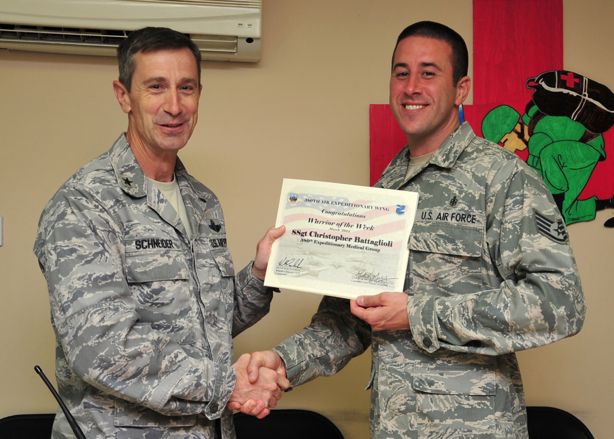 Air Force Brig. Gen. Kevin Schneider, 380th Air Expeditionary Wing commander, presents Air Force Staff Sgt. Christopher Battaglioli, 380th Expeditionary Medical Group Emergency Medical Technician, a warrior of the week certificate at an undisclosed location in Southwest Asia, March 19, 2014. Battaglioli is a native of Long Beach, Calif., and is deployed from Nellis Air Force Base, Nev. (U.S. Air Force photo by Tech. Sgt. Colleen Urban)
