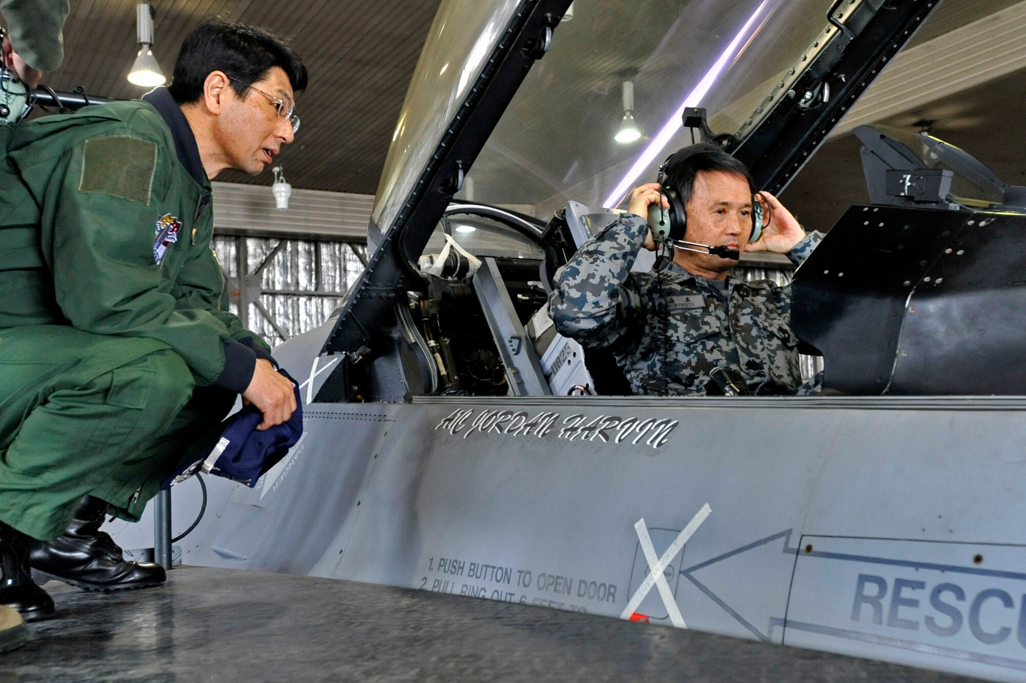 MISAWA AIR BASE, Japan -- Japan Air Self-Defense Force Lt. Gen. Tetsuo Morimoto, Northern Air Defense Force commander, adjust his headsets as JASDF Maj. Gen. Tomoyuki Ueda, NADF vice commander, looks on during a tour of an F-16 Fighting Falcon in Hangar 911, March 18, 2014. The NADF commanders had the opportunity to try out the F-16 Fighting Falcon’s targeting pod and learn about the munitions it’s capable of carrying. (U.S. Air Force photo/Staff Sgt. Tong Duong)