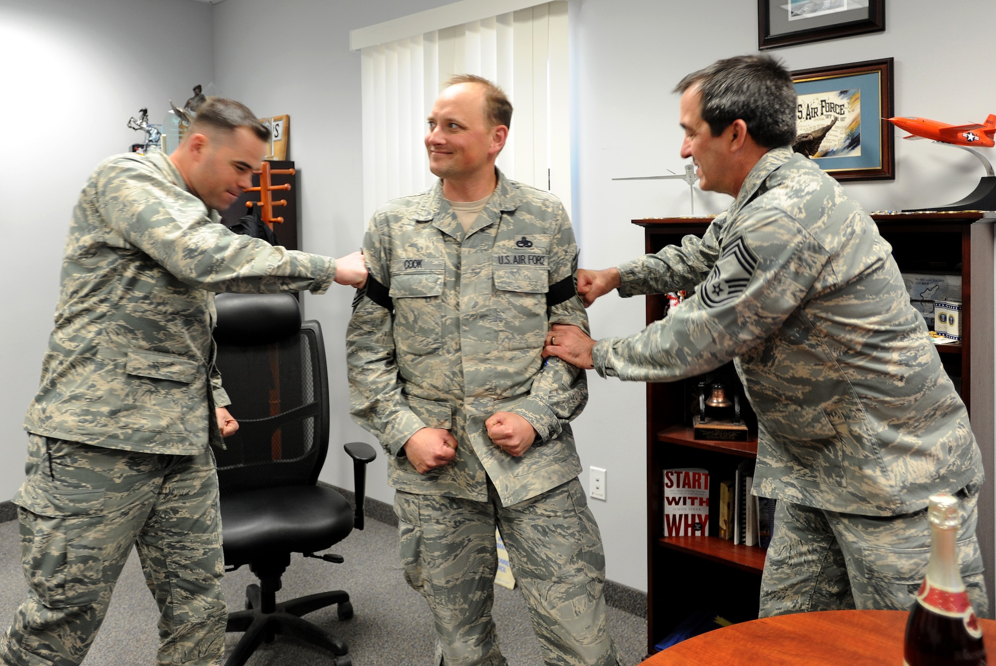 Maj. Eric Deturk, left, 799th Security Forces Squadron commander and Chief Master Sgt. Steven Bohannon, 799th Air Base Group superintendent, tack on Master Sgt. Steven Cook, 799th Security Forces Squadron first sergeant, after being selected for senior master sergeant. Leadership from the 432nd Wing/432nd Air Expeditionary Wing congratulated selectees and thier families from Creech and Nellis Air Force Bases at their homes. (U.S. Air Force photo by Senior Master Sgt. C.R.)