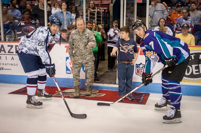 Col. Jeffrey DeVore, Joint Base Charleston commander, and Luke Murphy, ten-year old of Charleston, S.C., drop the ceremonial hockey puck March 22, 2014, during the South Carolina Stingrays Military Appreciation Night at the North Charleston Coliseum, S.C. Photographed (left) Jack Downing, South Carolina Stingrays Forward, and Eric Baier, Orlando Solar Bears Defenseman await the puck drop. (U.S. Air Force photo / Senior Airman Tom Brading)