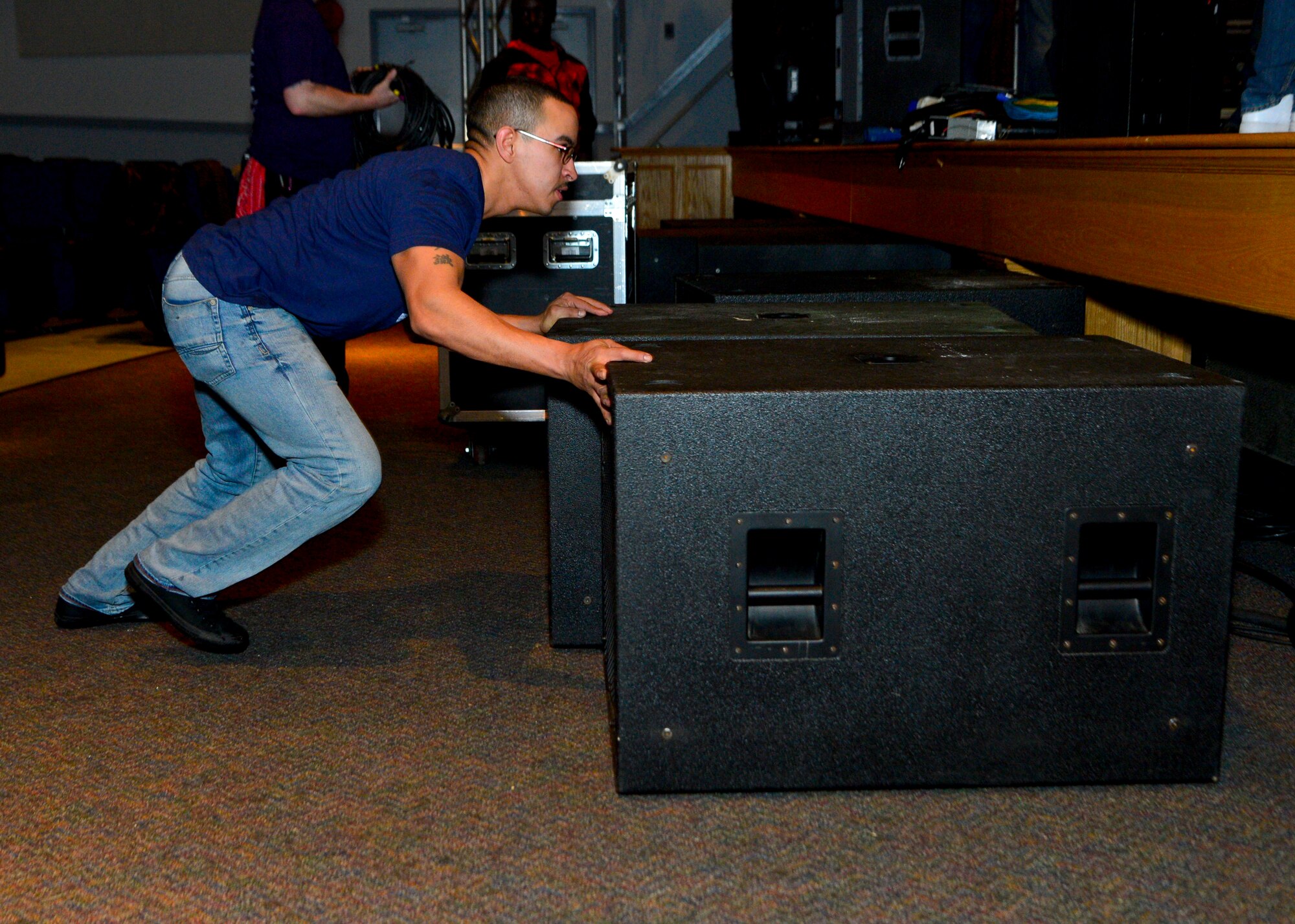 Staff Sgt. Chris Figueroa, 436th Aircraft Maintenance Squadron electronics environmental craftsman, pushes two large speakers underneath the stage during the teardown of the lighting, sound, and musical equipment March 19, 2014, inside the base theater on Dover Air Force Base, Del. Figueroa volunteered his time to help set up light and sound equipment for the Jana Kramer and Swon Brothers concert hosted by the USO. (U.S. Air Force photo/Airman 1st Class Zachary Cacicia)