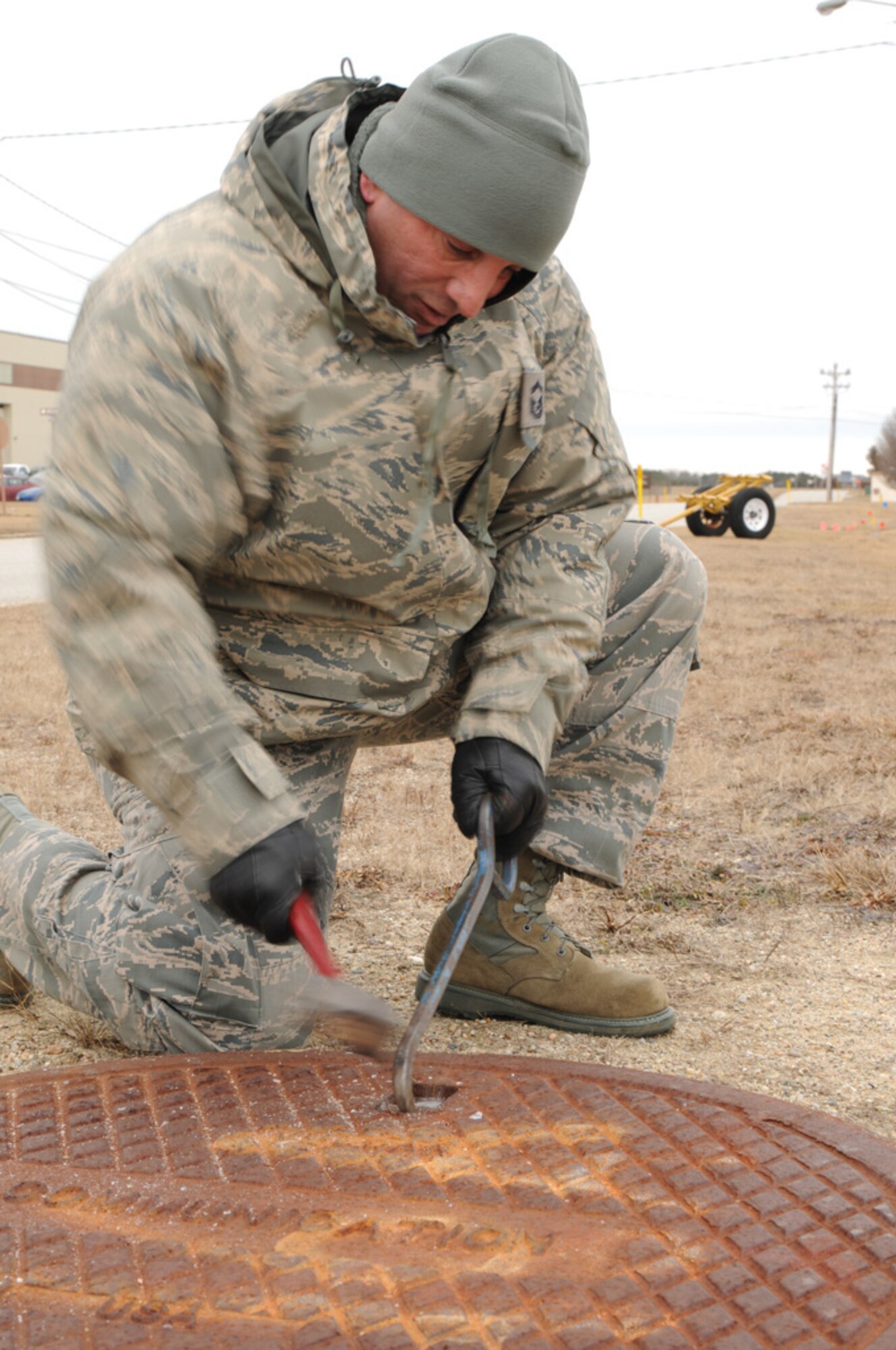 Senior Master Sgt. Jose Franco, from the 253rd Combat Communications Squadron, chips ice away from a manhole cover before gathering real-world data on the infrastructure of Otis Air National Guard Base during a GeoBase class on January 21, 2014. (National Guard photo by Master Sgt. Aaron Smith/Released)