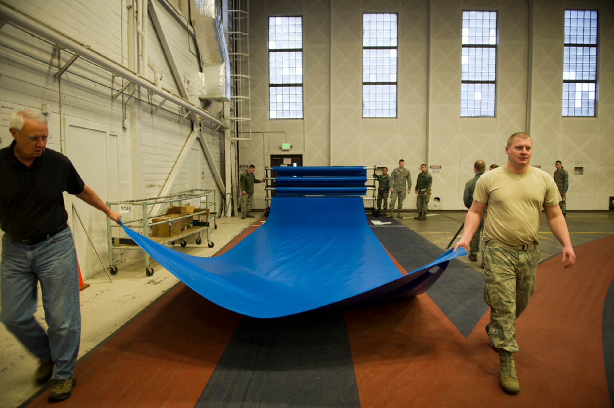 Thomas Lawson, director of the JBER-Elmendorf Fitness Center for the 673d Force Support Squadron, and Senior Airman Corby Wilson, 673d Communications Squadron radio frequency transmission systems journeyman, roll out a tarp to protect the indoor track at Hangar 5 on Joint Base Elmendorf-Richardson, Alaska, on March 17, 2014. Volunteers from many JBER units prepared temporary living quarters for U.S. armed forces in support of exercise Alaska Shield 2014. (U.S. Air Force photo/Airman 1st Class Omari Bernard)