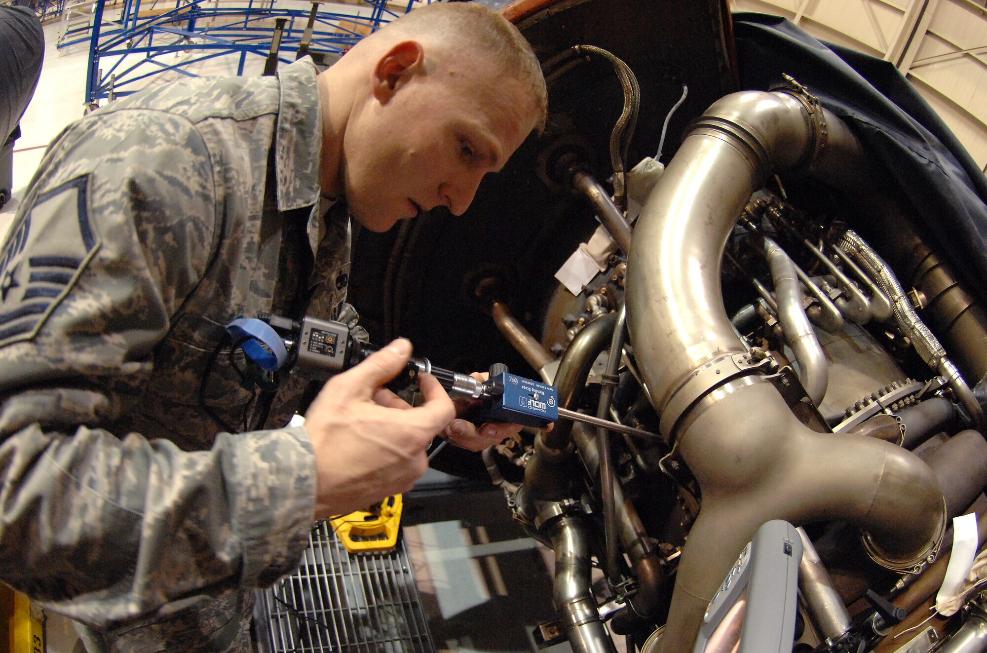 Master Sgt.  Steve Pakusch, 55th Aerospace Maintenance Squadron production superintendent, demonstrate how the Wolf Blending Scope is used to fix damaged compressor blades inside an aircraft hangar at Offutt Air Force Base, Neb. March 19.. An adjustable grinding tool attached to a rod about three feet long is inserted through a one-inch port on the side of an aircraft engine, which allows Pakusch to grind down irregularities without removing the engine from the aircraft and taking it apart. A light on the end of the scope along with a camera provide a high quality video feed to an external monitor, necessary for the repairs. (U.S. Air Force photo by Delanie Stafford/Released)