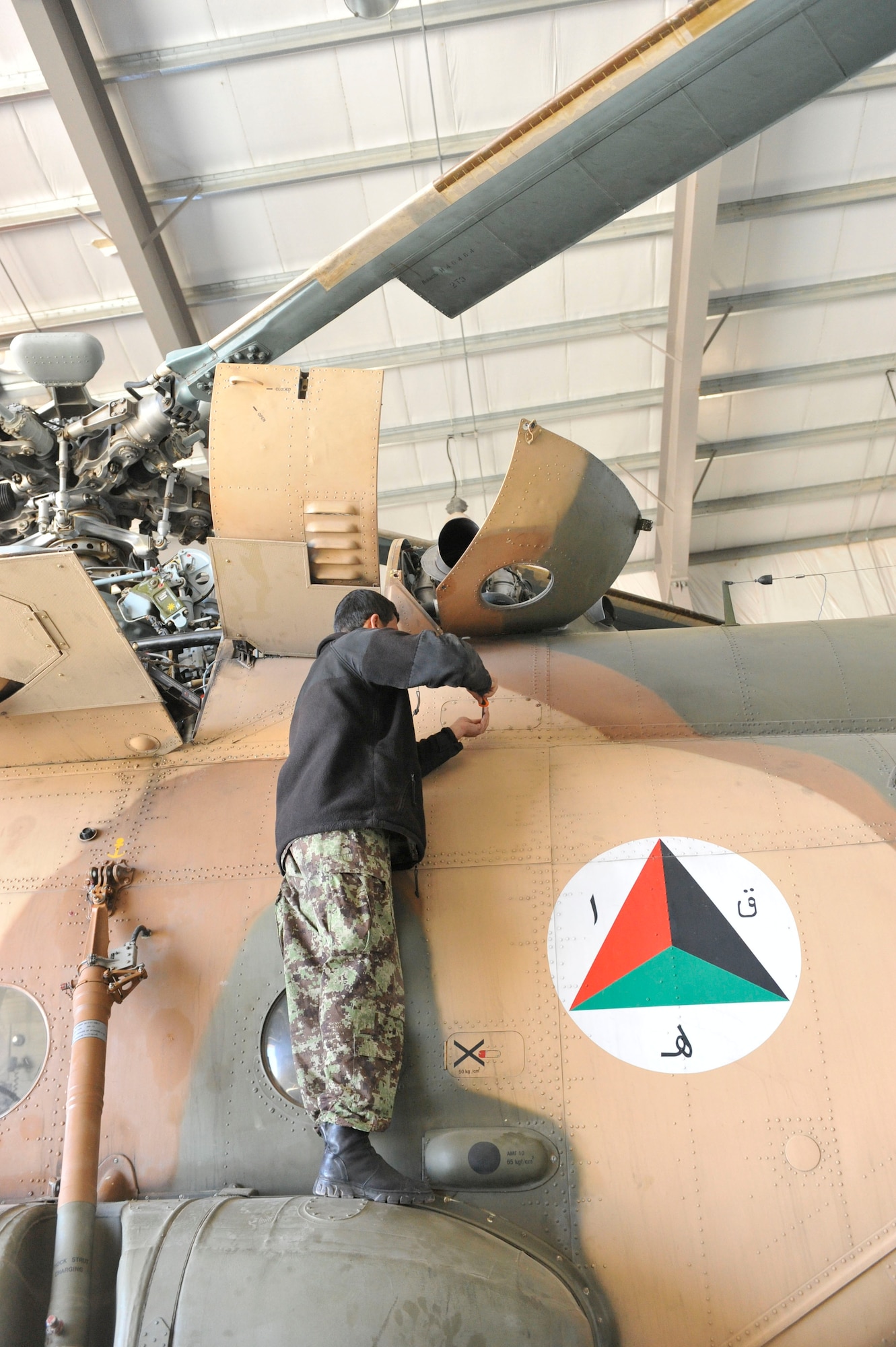 An Afghan aviation maintenance student removes a panel while performing maintenance on an Mi-17 helicopter at Shindand Airfield, Afghanistan, March 10, 2014. U.S. military advisors are training Afghan military members to fly and maintain aircraft at Shindand.(U.S. Air Force photo by Senior Master Sgt. Gary J. Rihn/Released)