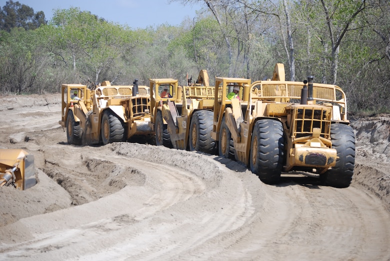 Heavy earth-moving equipment form a three-vehicle train to remove material near the San Luis Rey River to construct a bypass channel designed to reestablish a portion of the river to its historical hydrologic and vegetative condition.