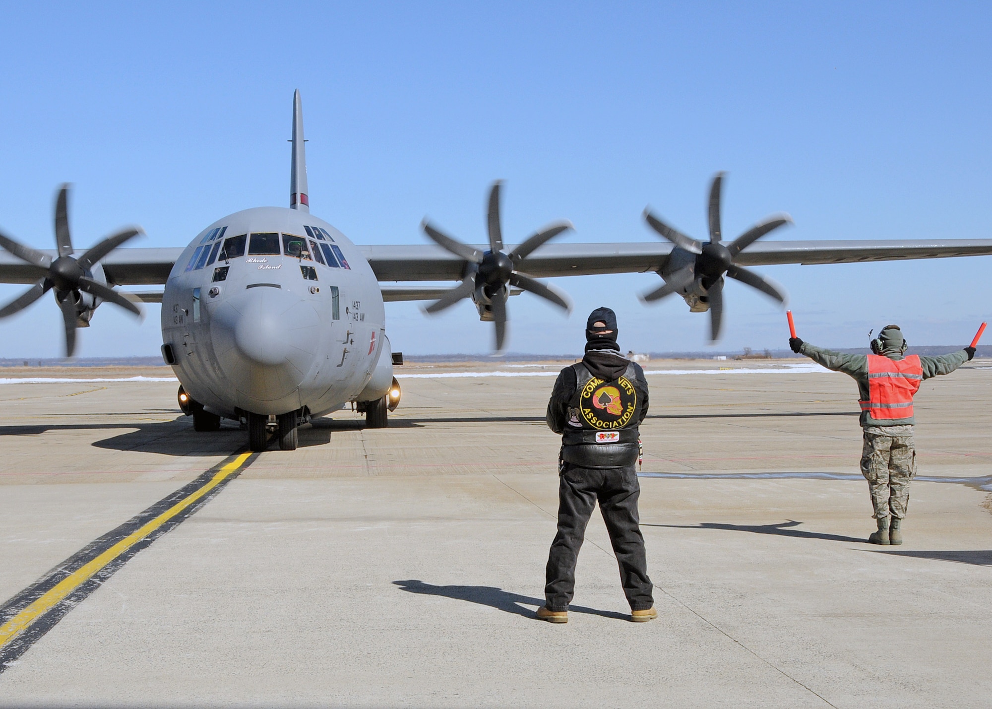 A member of the 143d Maintenance Group marshalls in a C-130J Super Hercules carrying members of the 143d Airlift Wing returning from a deployment to Kuwait in support of Operation Enduring Freedom while a member of the Combat Veterans Motorcycle Association looks on. National Guard Photo by Master Sgt Janeen Miller (RELEASED)