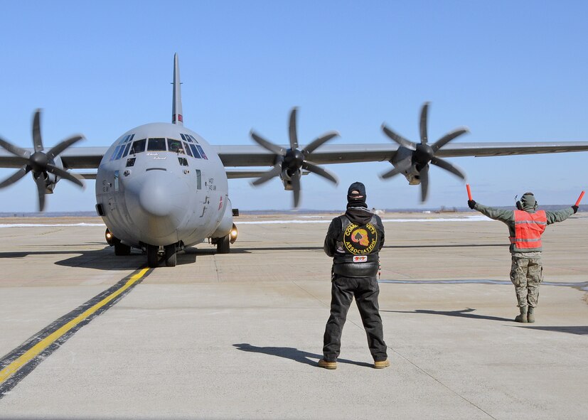 A member of the 143d Maintenance Group marshalls in a C-130J Super Hercules carrying members of the 143d Airlift Wing returning from a deployment to Kuwait in support of Operation Enduring Freedom while a member of the Combat Veterans Motorcycle Association looks on. National Guard Photo by Master Sgt Janeen Miller (RELEASED)