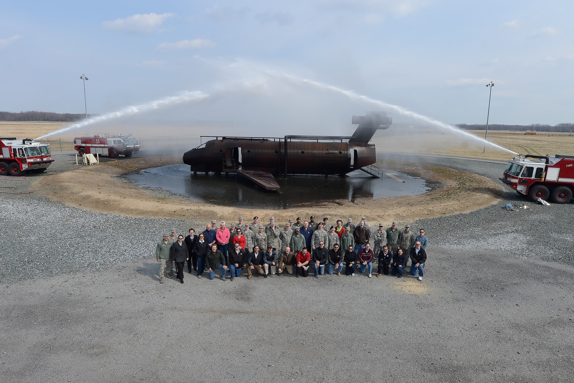The 2014 Dover Air Force Base Honorary Commanders pose with military members for a group photo in front of the 436th Civil Engineer Squadron, Fire Department's, aircraft fire training device March 21, 2014, at DAFB, Del. Close inspection reveals most people have real or fake mustaches as part of the 'Mustache March' challenge given by Air Force Chief of Staff, Gen. Mark Welsh. (U.S. Air Force photo/Greg L. Davis)