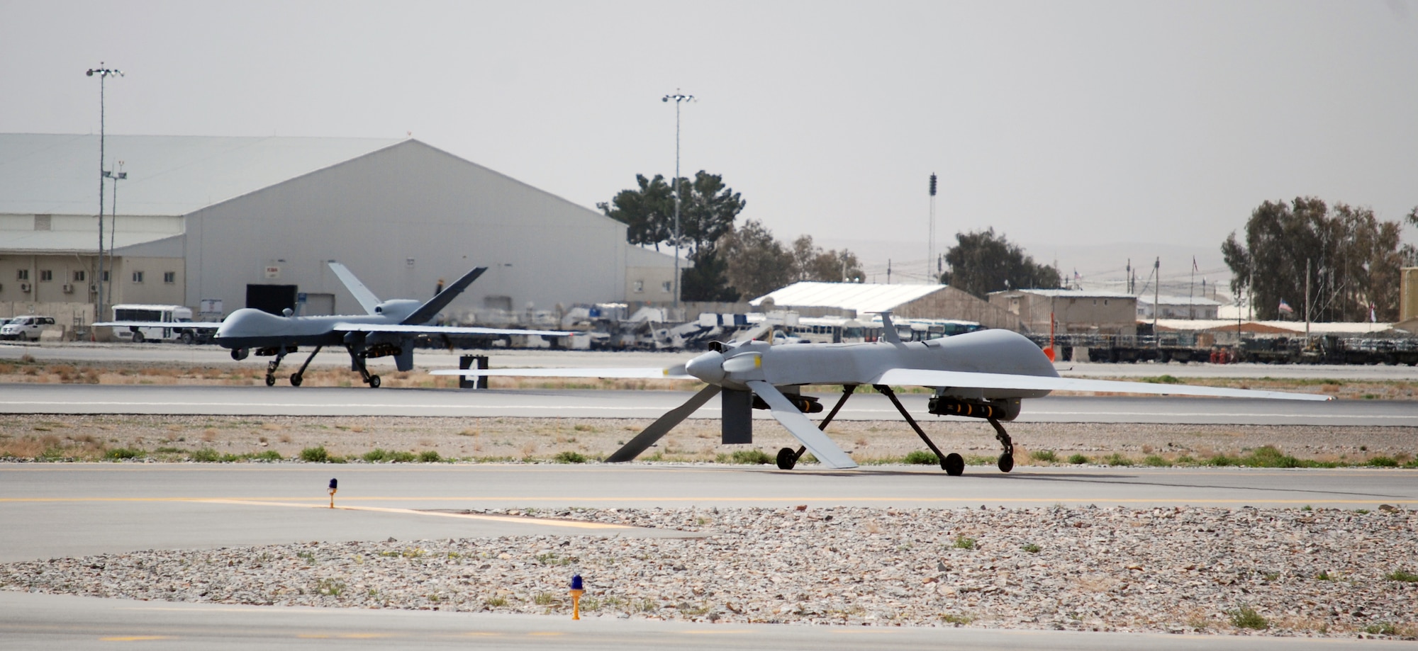 An MQ-1 Predator taxis as an MQ-9 Reaper lands at Kandahar Airfield, March 20, 2014. The MQ-1 and MQ-9 are assigned to and operated by the 451st Air Expeditionary Group. (U.S. Air Force photo by Capt. Brian Wagner/Released) (Image was cropped to emphasize aircraft.)