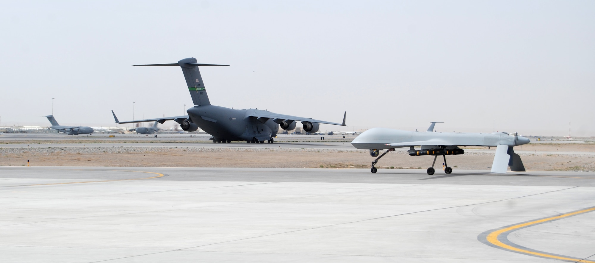 An MQ-1 Predator waits for a taxiing C-17 Globemaster III at Kandahar Airfield, March 20, 2014. The MQ-1 is assigned to and operated by the 451st Air Expeditionary Group. (U.S. Air Force photo by Capt. Brian Wagner/Released) (Image cropped to emphasize aircraft.)