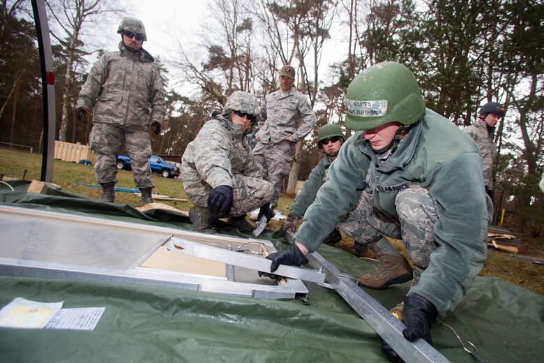 A1C Wesley Diefenbach and Senior Airman Andrew Bracken, 175th Civil Engineer Squadron, Maryland Air National Guard assists their team members in constructing a tent during a practical application portion of the Silver Flag exercise, March 24, 2014,Ramstein Air Base, Germany. The Silver Flag exercise simulates training relevant to building and beddown of a bare base operation in a deployed environment. (U.S. Air National Guard photo by Master Sgt. Gareth Buckland/Released)