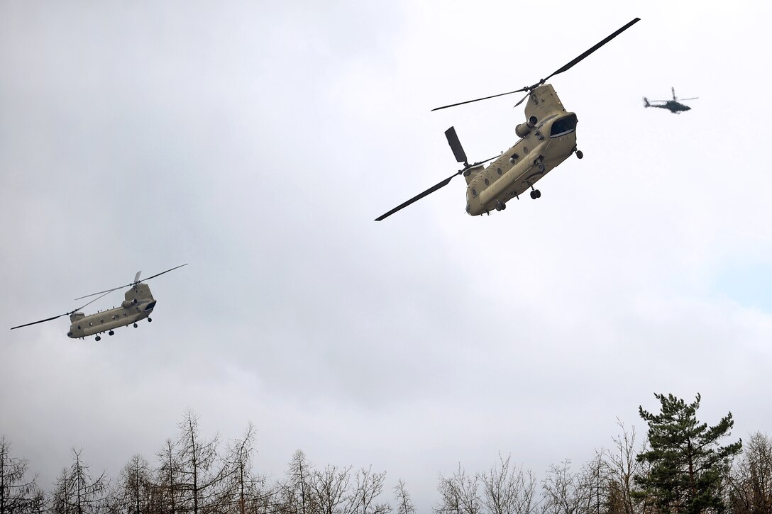 U.S. Army CH-47 Chinook helicopters lift off for an air assault mission while a AH-64 Apache helicopter provides aerial security at the 7th Army Joint Multinational Training Command's Hohenfels Training Area, Germany, March 19, 2014.