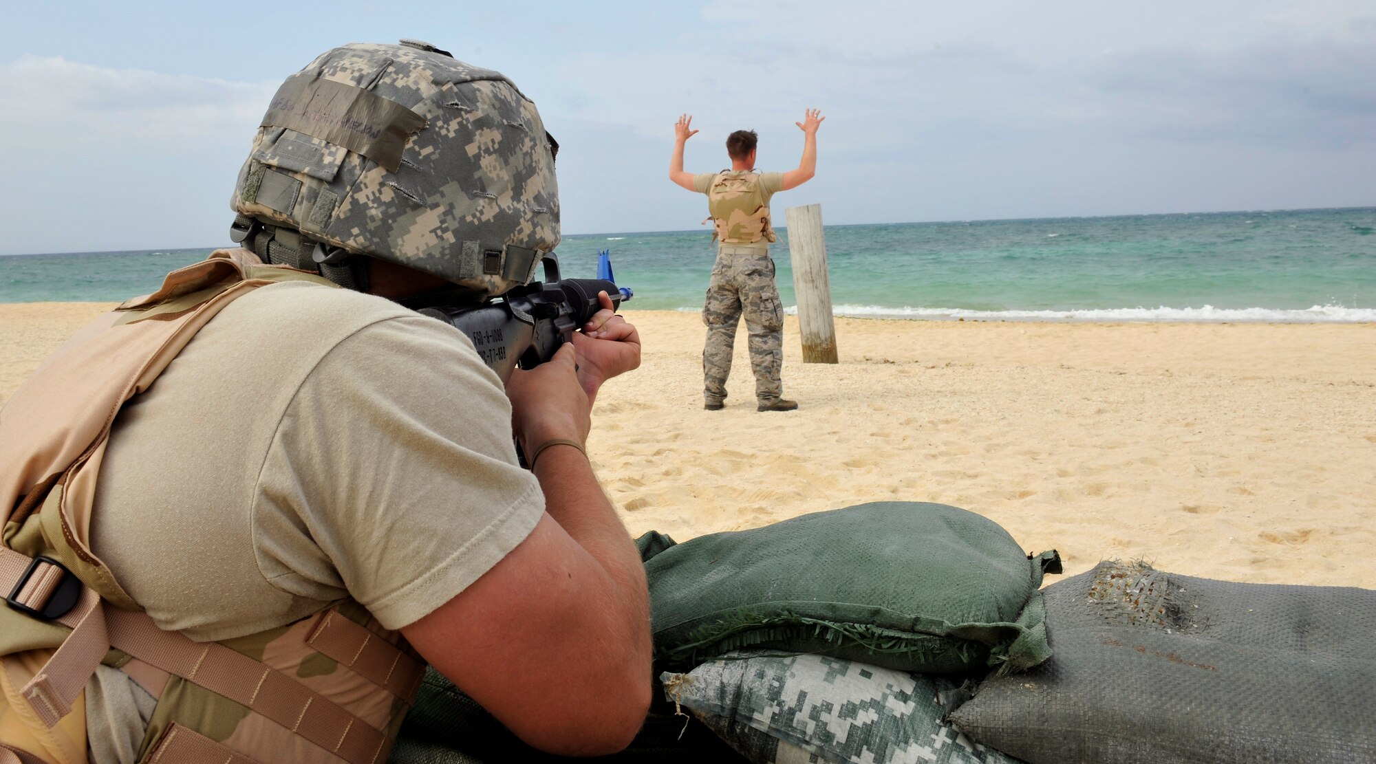 U.S. Air Force Senior Airman Jarrett Welton aims a rubber M-16 A2 rifle at Senior Airman Kollin Ailworth during Defensive Fighting Position training on Torii Beach, Japan, March 20, 2014. Airmen frequently conduct training to prepare for real-world scenarios and enhance their combat capabilities. Welton and Ailworth are both 18th Civil Engineer Squadron Heating, Ventilation, Air Conditioning and Refrigeration journeymen. (U.S. Air Force photo by Naoto Anazawa)