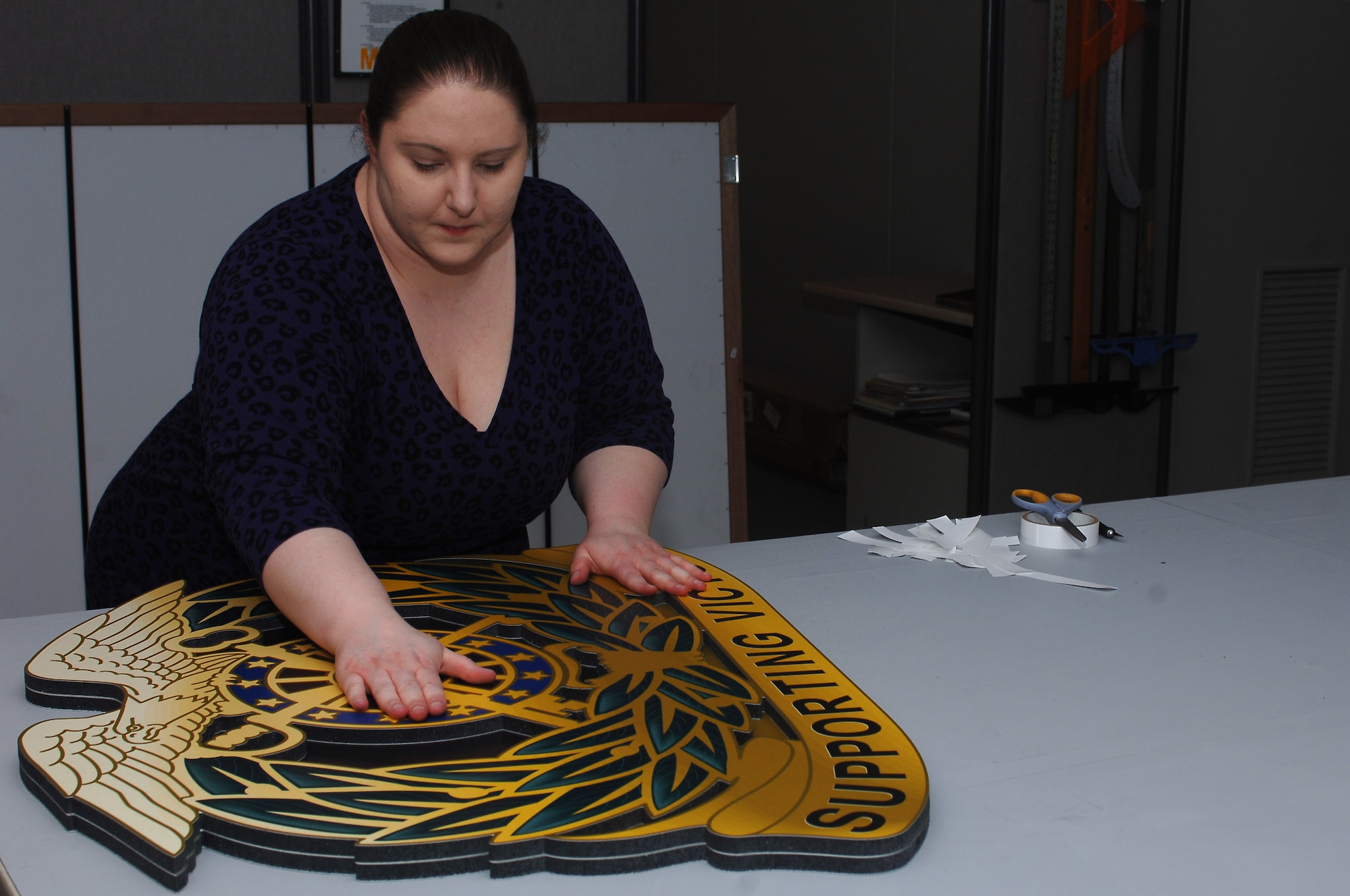 Gwyn Giacomo, Enterprise Multimedia Center graphic designer, assembles a layered unit logo at Fort Eustis, Va., March 25, 2014. The graphics department at EMC can design, print and install morale and training aids, such as 80-foot-by-100-foot floor maps, unit logos and range targets. (U.S. Air Force photo by Senior Airman Teresa J.C. Aber/Released)