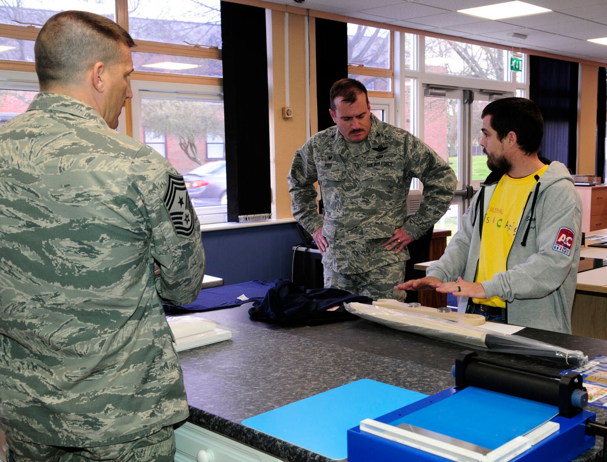 Stephen Fournier, right, 100th Force Support Squadron Arts and Crafts Center engraver from Jacksonville, N.C., shows U.S. Air Force Col. Kenneth T. Bibb Jr., center, 100th Air Refueling Wing commander, and U.S. Air Force Chief Master Sgt. Tracy Jones, 100th ARW command chief, examples of the services the arts and crafts center offers March 25, 2014, at the grand opening of the new facility within the Bob Hope Community Center on RAF Mildenhall, England. The new center's services offered include custom framing, embroidery and engraving, and hours of operation are 9 a.m. to 4 p.m. Monday to Friday. (U.S. Air Force photo by Karen Abeyasekere/Released)