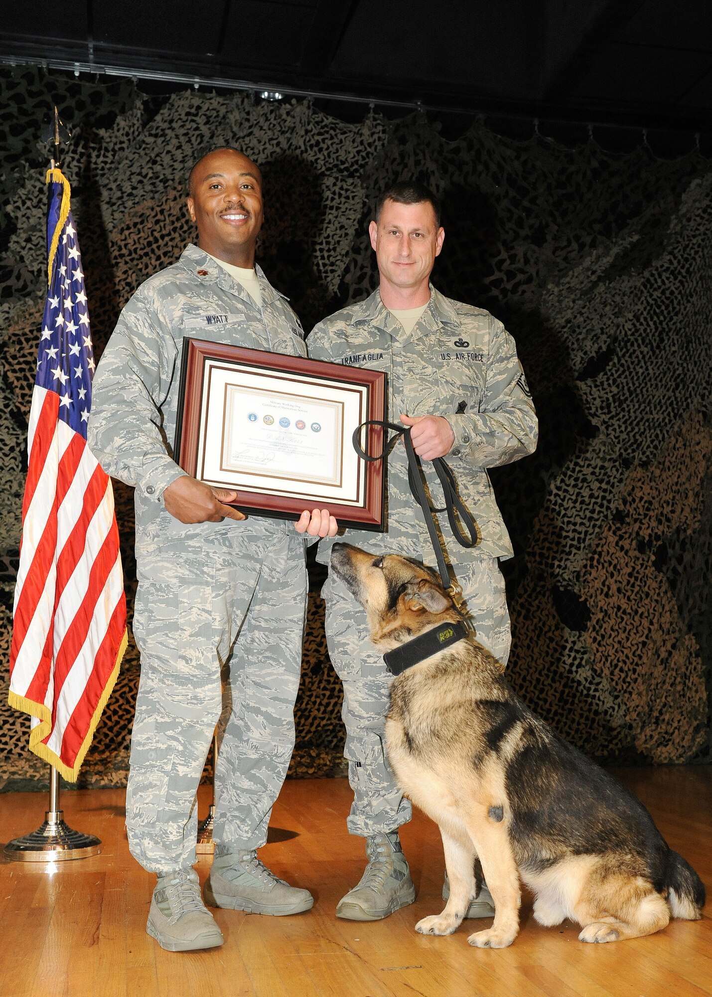 Maj. Wyatt Lawrence, Jr. (left), 65th Security Forces Squadron commander, presents a Military Working Dog Certificate of Meritorious Service to MWD Dan upon his retirement from the U.S. Air Force March 25, 2014. MWD Dan, a nine-year U.S. Air Force veteran, served as a devoted team member to 10 MWD handlers as a narcotics detector on Lajes Field, Azores. He is now adopted by Senior Master Sgt. Jason Tranfaglia (right), 65th SFS manager. (U.S. Air Force photo by Guido Melo/Released)