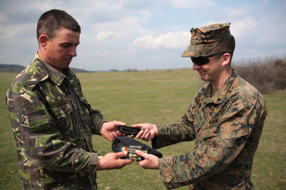 Corporal Patrick Phelan, mortarman, weapons company, 3rd Battalion, 8th Marines, assigned to Black Sea Rotational Force 14 exchanges a gift with a Romanian service member during a combined maneuver live fire exercise at Babadag Training Area, Romania, 26 March, 2014.  During exercises, exchanging gifts among service members from different countries signifies comradeship. Black Sea Rotational Force 14 is a task force of Marines and sailors with the mission to sustain positive relationships with partner nations uphold regional stability and increase military operational capabilities while also proving the ability for rapid crisis response in the Black Sea, Balkan and Caucasus regions of Eastern Europe. (Official Marine Corps photo by Staff Sgt. Tanner M. Iskra, BSRF Combat Camera/Released)