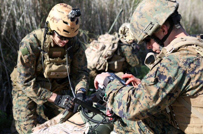 While HM2 Kristofer Baskett (left) assesses the Sailor’s simulated wounds, Sgt. Danny Pereira (right) monitors his vital signs with the Tempus Pro portable vital signs monitor. Pereira was able to transmit the vital signs as well as pictures and video of the injuries back to the Battalion Aid Station through the Tempus Pro.