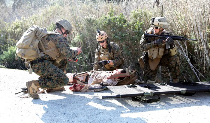 Sgt. Danny Pereira (left) and HM2 Kristofer Baskett (center) continue to monitor the status of the injured Sailor and treat his simulated wounds. Baskett is able to adjust treatment based on direction from the medical provider at the Battalion Aid Station. The Tempus Pro allows the on scene medical provider to communicate through voice or text to the next level of care like a Battalion Aid Station.