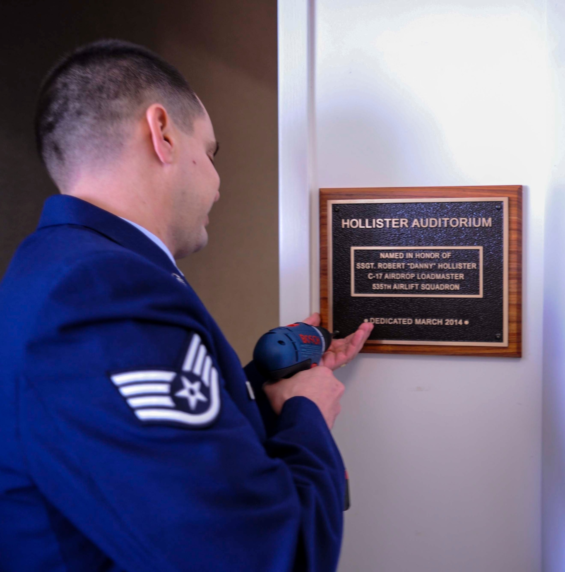 Staff Sgt. Keith Roscoe, 535th Airlift Squadron loadmaster, hangs a plaque outside the Hollister Auditorium on Joint Base Pearl Harbor-Hickam, Hawaii, March 28, 2014. The auditorium is dedicated to fallen comrade, Staff Sgt. Robert “Danny” Hollister who was a 535th AS loadmaster here. (U.S. Air Force photo/Tech. Sgt. Terri Paden)