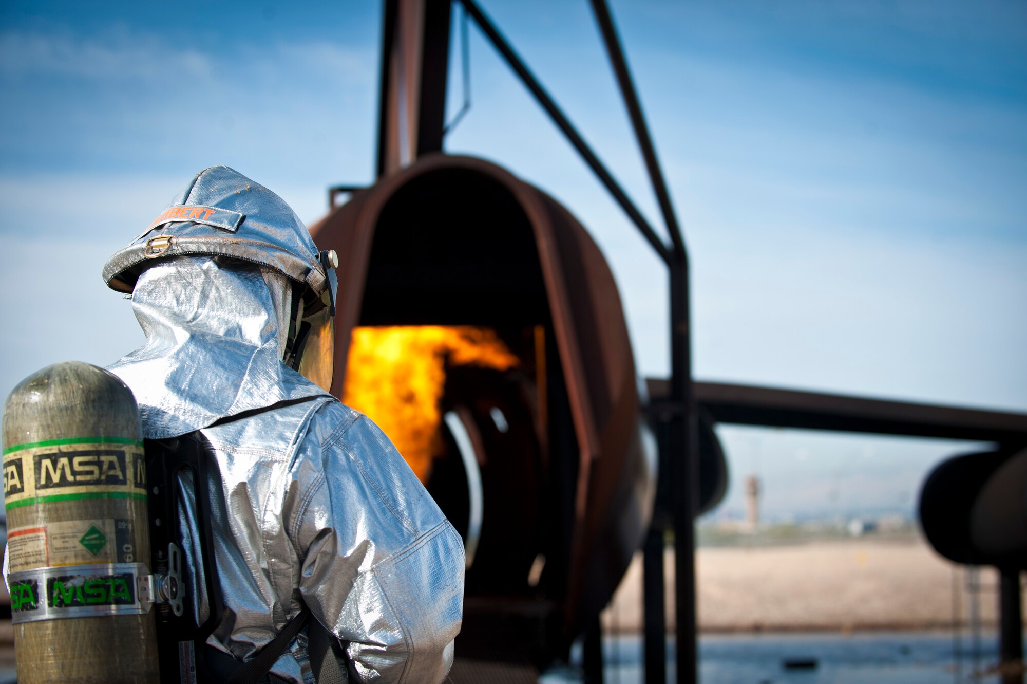 Carl Lambert, 99th Civil Engineer Squadron fire chief, leads the way toward a simulated aircraft interior fire during an exercise on the aircraft burn trainer March 27, 2014 at Nellis Air Force Base, Nev.  The Nellis aircraft burn trainer was built with several ignition points on different parts of the aircraft to create realistic scenarios for firefighters. (U.S. Air Force photo by Airman 1st Class Joshua Kleinholz)