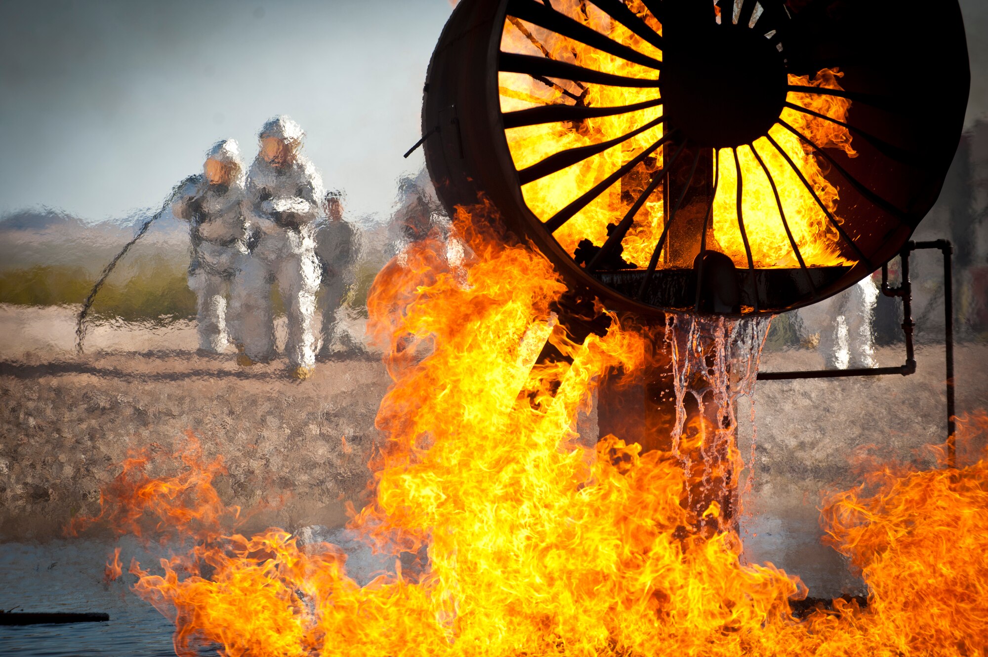 Firefighters from the 99th Civil Engineer Squadron, approach an aircraft burn trainer during a training certification exercise March 27, 2014 at Nellis Air Force Base, Nev.  99th CES firefighters train constantly to maintain a high level of readiness, and are expected to respond rapidly in the event of an aircraft emergency. (U.S. Air Force photo by Airman 1st Class Joshua Kleinholz)