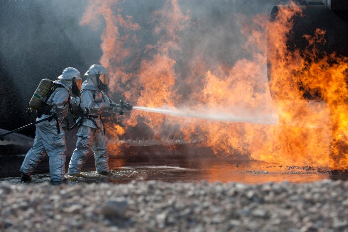Firefighters assigned to the 99th Civil Engineering Squadron battle blazes during a live fire training exercise at the aircraft burn trainer March 27, 2014, at Nellis Air Force Base, Nev. The firefighters suppress the flames with a hose attached to a rapid intervention vehicle. The RIV can deliver between 1,300 and 1,500 gallons of water per minute. (U.S. Air Force photo by Airman 1st Class Thomas Spangler)