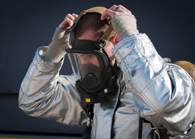 Airman 1st Class Cameron Fox, 99th Civil Engineering Squadron firefighter, dons his mask before a fire suppression exercise at the aircraft burn trainer March 27, 2014, at Nellis Air Force Base, Nev. The 99th CES firefighters are required to undergo live fire suppression training twice a year. The training sessions are done during day and  night operations. (U.S. Air Force photo by Airman 1st Class Thomas Spangler)