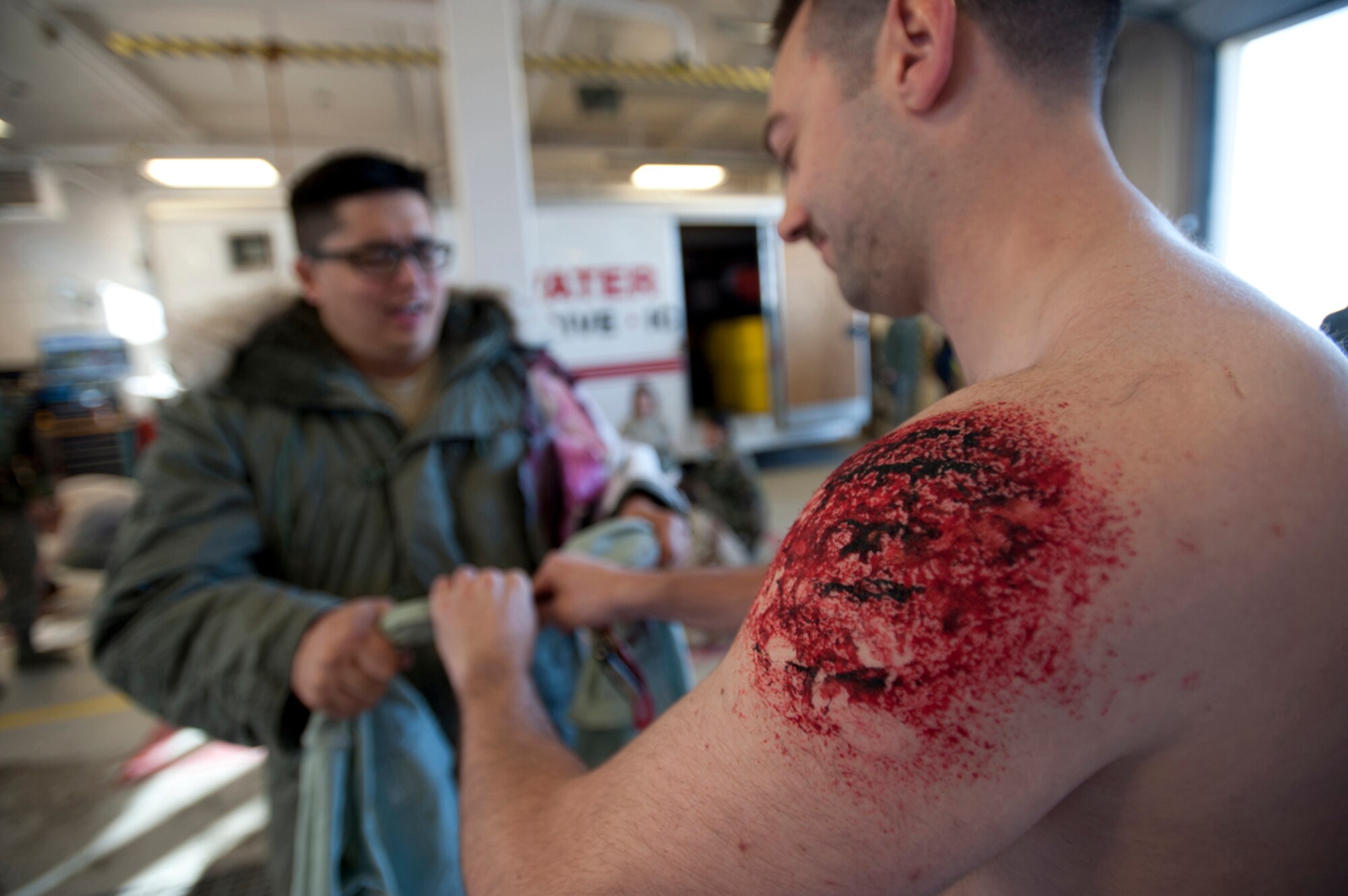 Senior Airman Scott Ellis, left, and Airman Hilde Garrett tear up Garrett’s shirt to make bandages for their simulated wounds after a simulated earthquake emergency scenario at Joint Base Elmendorf-Richardson, Alaska, March 27, 2014. The Mission Assurance Exercise 14-3 is part of the overall Alaska Shield disaster response preparedness and response exercise. (U.S. Air Force photo/Staff Sgt. Robert Barnett)