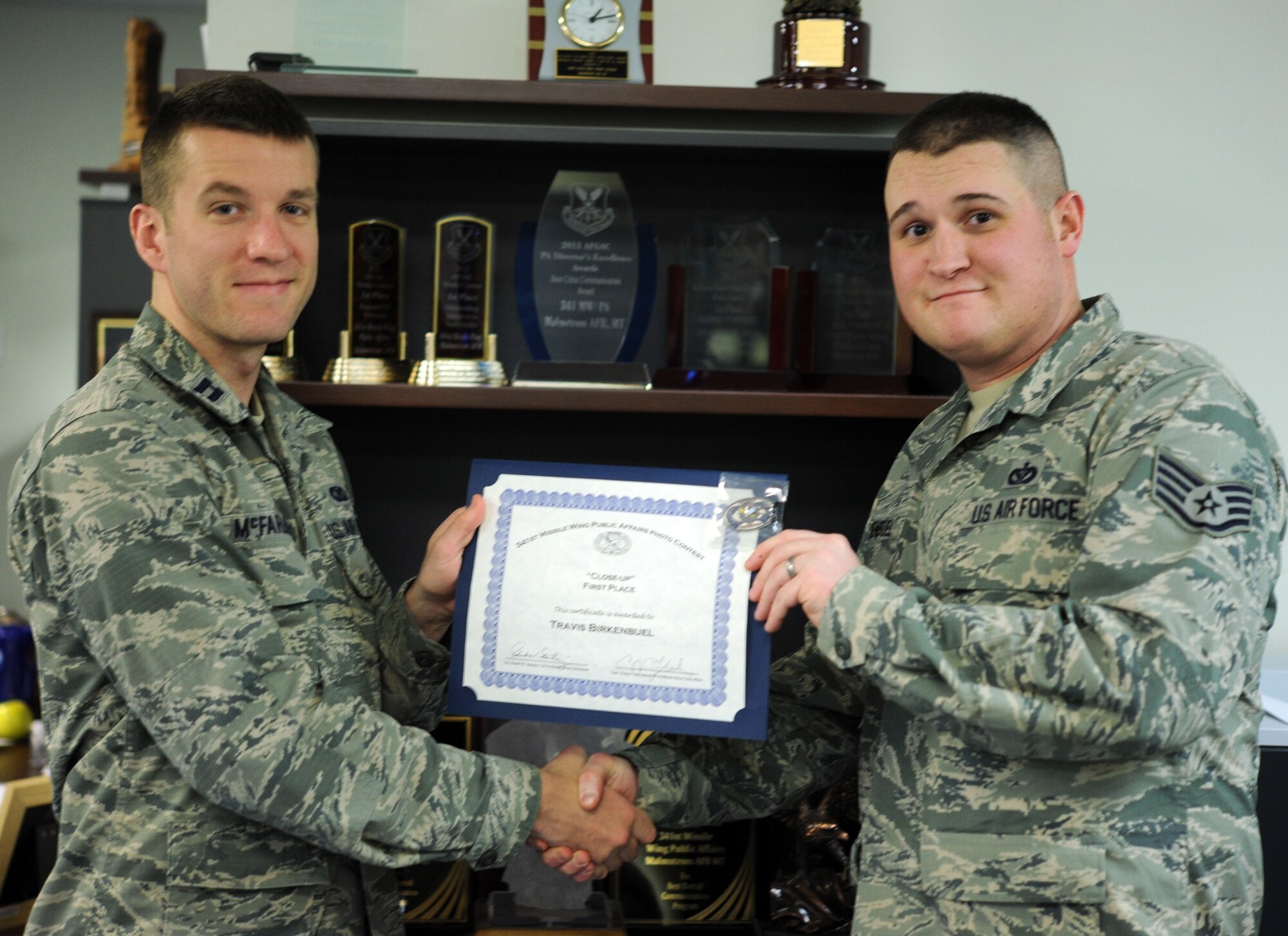 Staff Sgt. Travis Birkenbuel, 341st Civil Engineer Squadron NCO in charge of heavy requirements and optimization, receives a certificate and coin from Capt. Chase McFarland, 341st Missile Wing Public Affairs deputy chief, after winning the most recent 341st MW PA Quarterly Amateur Photo Contest. The photo expressed the theme, "Close-ups," as it shows an intimate view of frost embracing a barbed-wire fence on a ranch near Wolf Creek, Mont. (U.S. Air Force photo/Airman 1st Class Joshua Smoot)