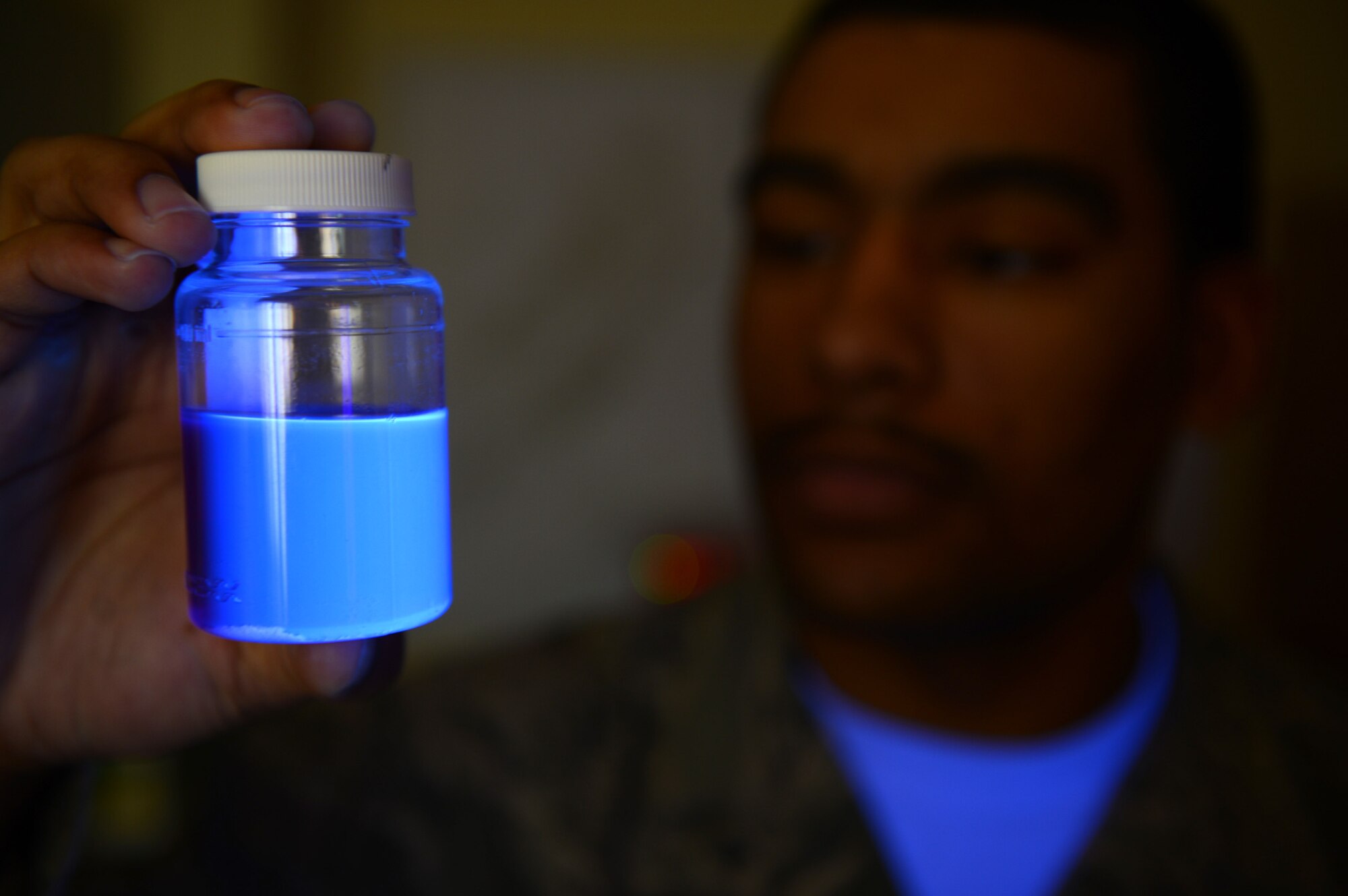 U.S. Air Force Airman 1st Class Bruce Moore, 52nd Aerospace Medicine Squadron bioenvironmental technician from Kansas City, Mo., examines a water sample under a black-light at Spangdahlem Air Base, Germany, March 28, 2014. Colilert is added to the water sample to detect the presence of bacteria. If bacteria is present, the water will glow under a black-light. (U.S. Air Force photo by Airman 1st Class Kyle Gese/Released)