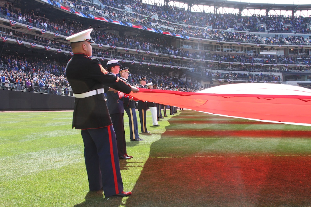 Sgt. Marco Velarde, a Marine recruiter at Recruiting Substation Smithtown, Recruiting Station New York, holds the corner of the flag during an unfurling at the New York Mets season opener game against the Washington Nationals at Citi Field March 31.
