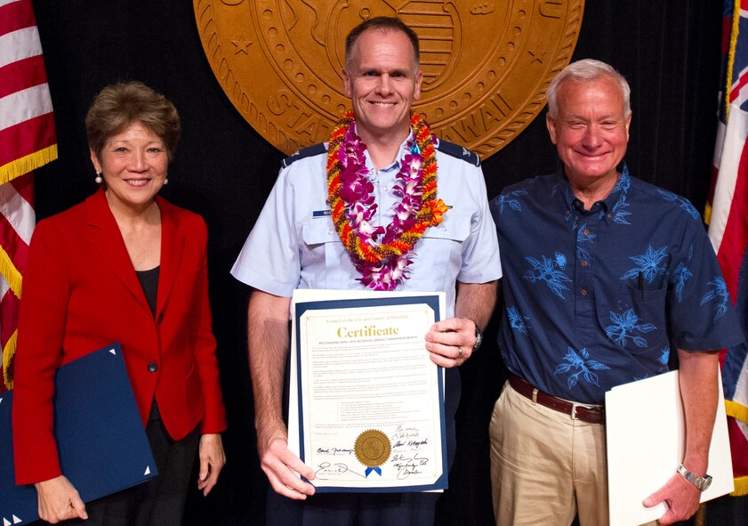 Col. Johnny Roscoe, 15th Wing Commander, Kirk Caldwell, the Mayor of Honolulu, and Carol Fukunaga, a Honolulu City Councilmember, present a certificate designating April as Sexual Assault Awareness Month at a ceremony in Honolulu 27 March.