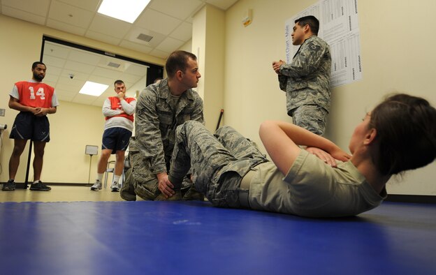 Airman 1st Class Justing Guerreso, Senior Airman Guinevere Running Wolf and Tech. Sgt. Juan Hernandez demonstrate and brief Airmen how to do proper sit-ups during the physical fitness test at Fairchild Air Force Base, Wash., March 27, 2014. Both Running Wolf and Hernandez are from the 92nd Force Support Squadron and Guerreso is from the 92nd Air Refueling Wing Judge Advocate. (U.S. Air Force photo by Airman 1st Class Janelle Patiño/Released)
